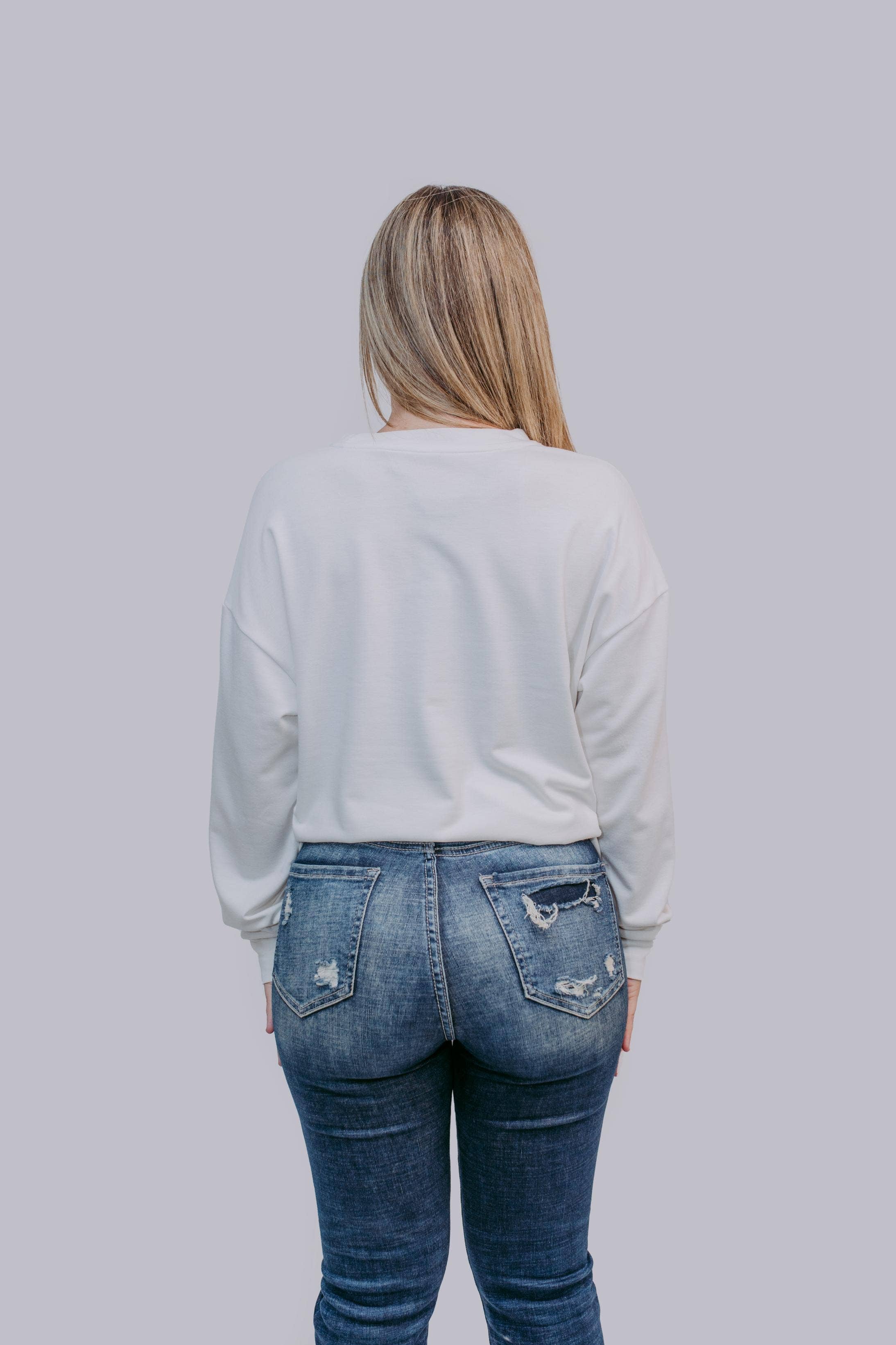 Person wearing a light gray sweater and blue jeans against a plain background