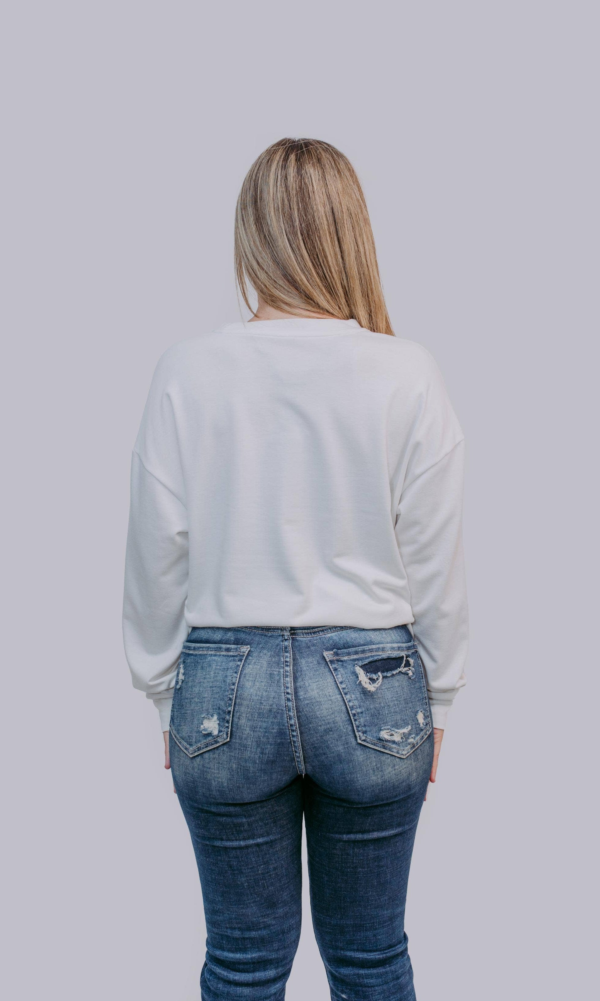 Person wearing a light gray sweater and blue jeans against a plain background