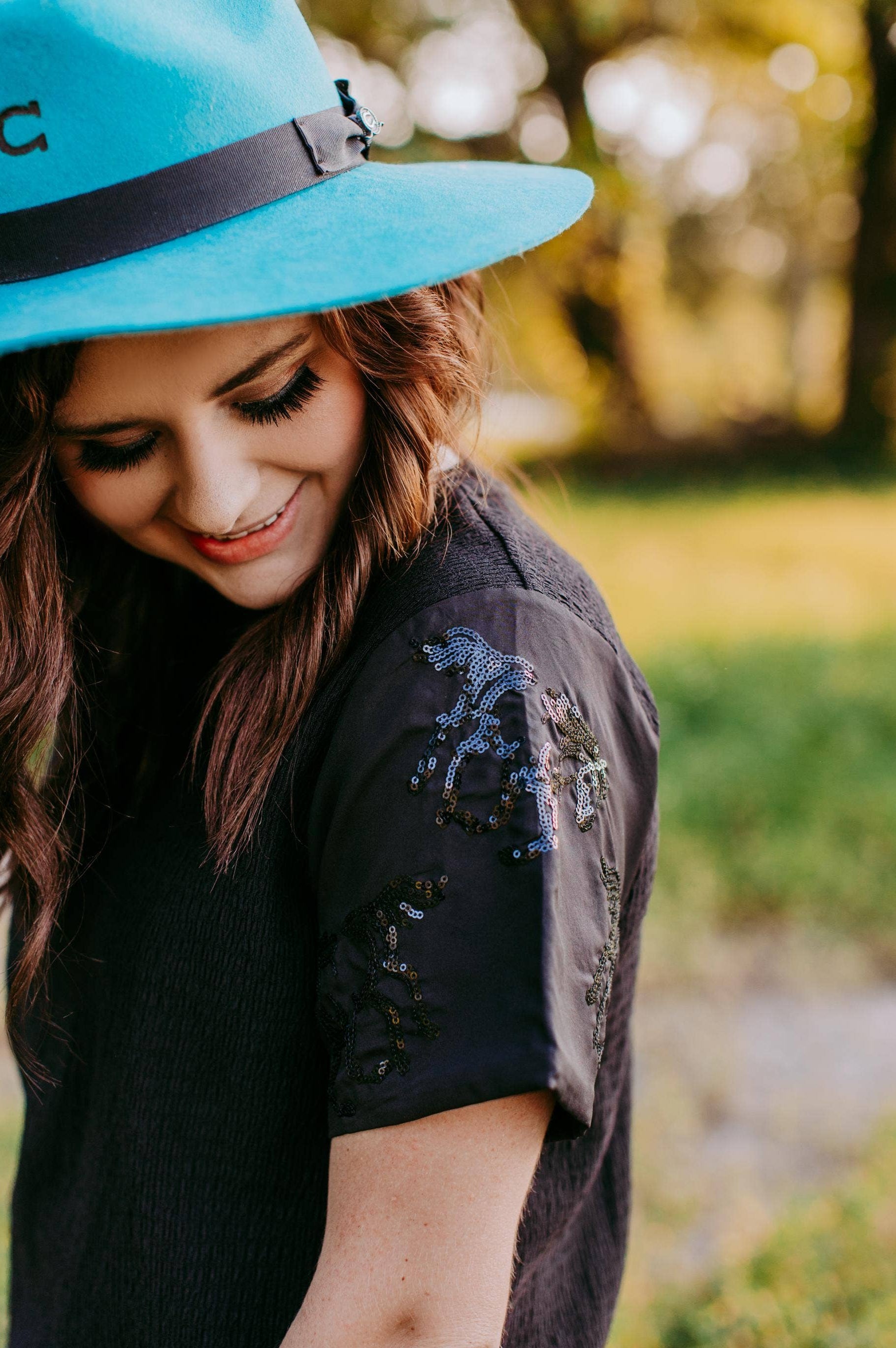 Woman wearing a blue hat and black shirt with horse sequin details