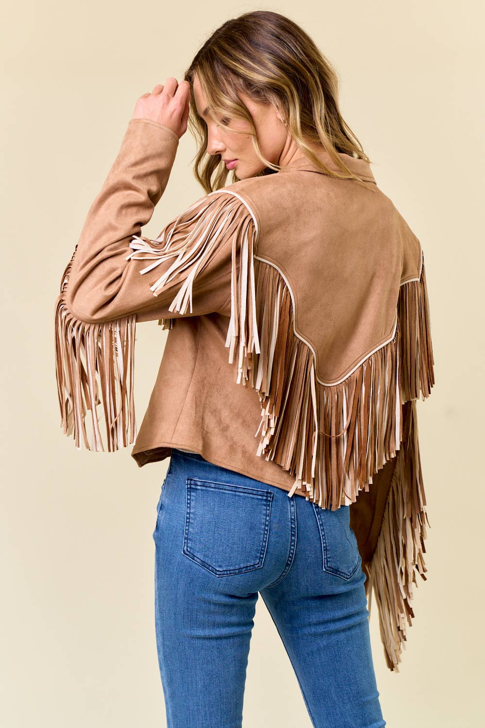 Woman wearing a brown suede jacket with fringe details on a beige background
