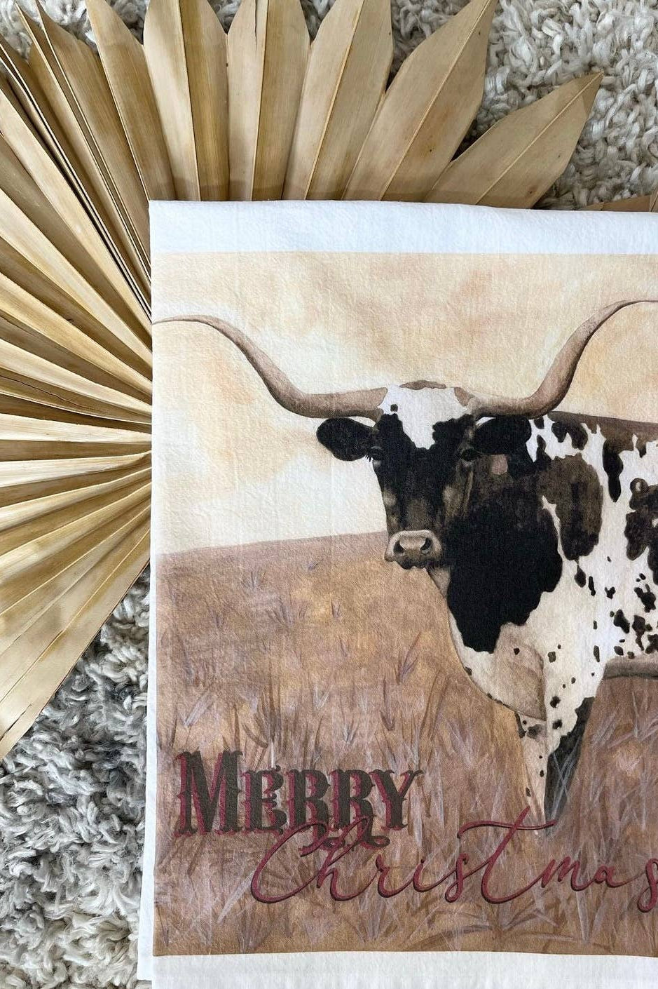 Kitchen towel with a longhorn cow illustration and 'Merry Christmas' text, surrounded by decorative elements.