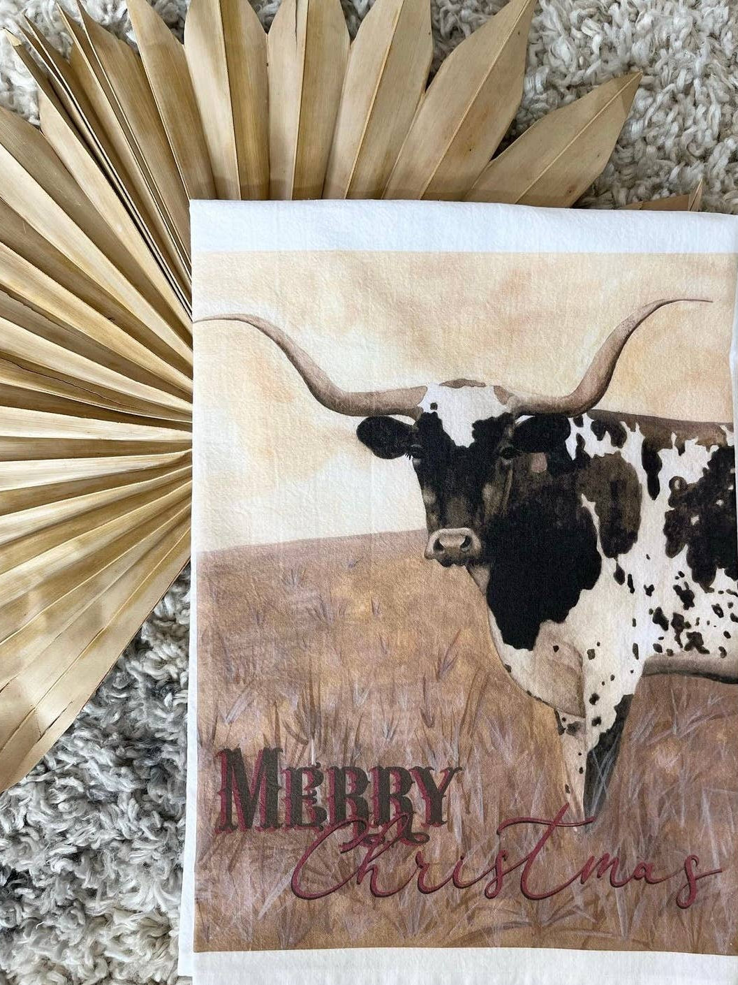 Kitchen towel with a longhorn cow illustration and 'Merry Christmas' text, surrounded by decorative elements.