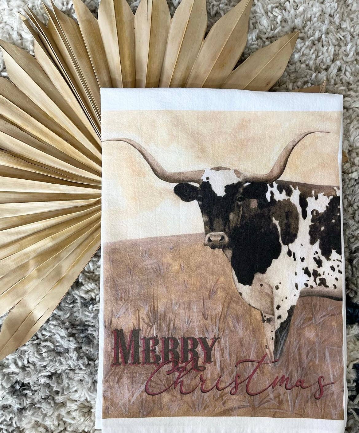 Kitchen towel with a longhorn cow illustration and 'Merry Christmas' text, surrounded by decorative elements.