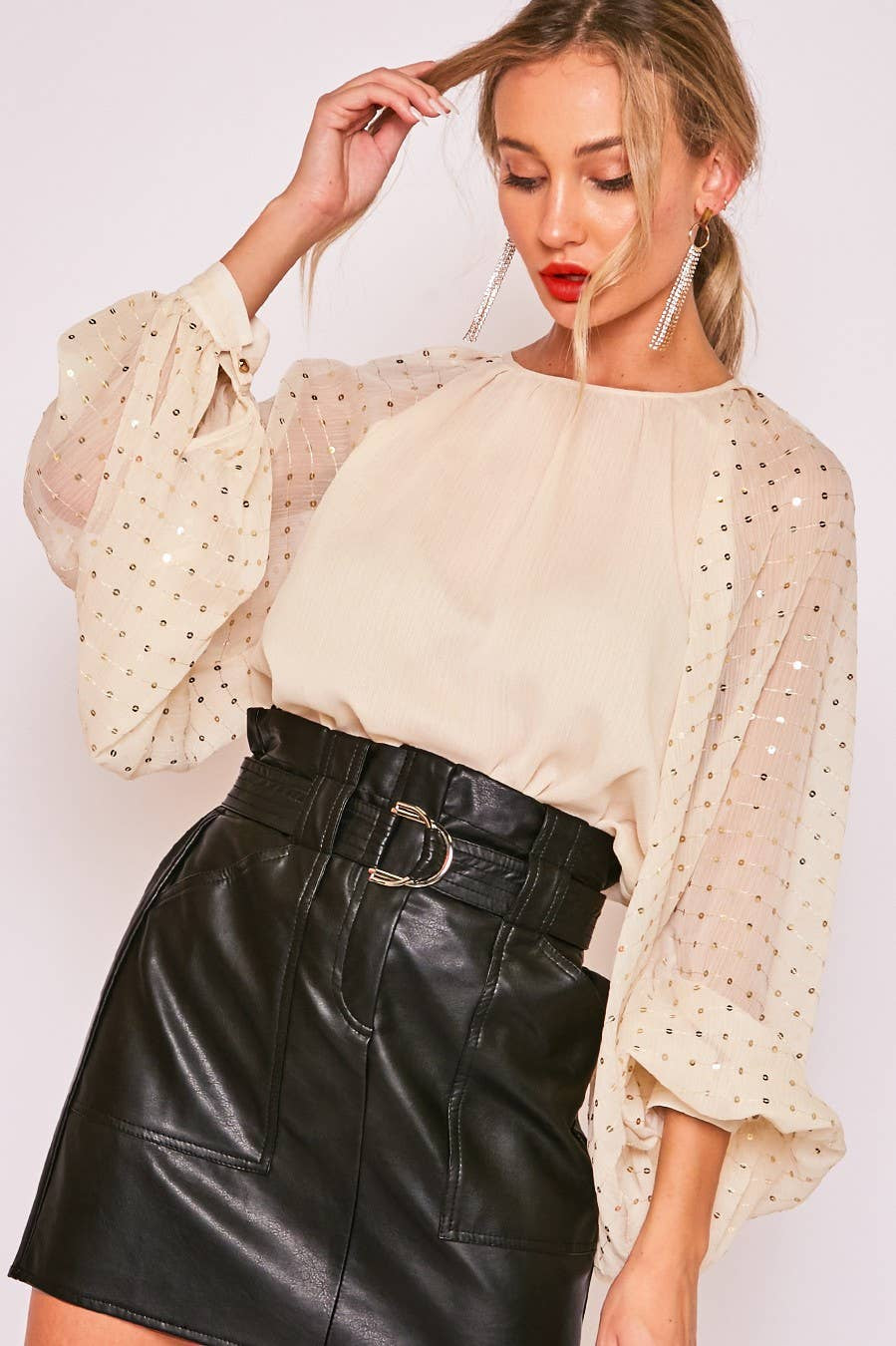 Woman wearing a beige blouse with sheer sleeves and a black leather skirt on a white background