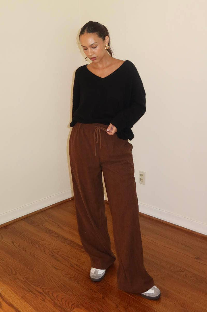 A model wearing wide leg brown pants with a drawstring waist and a white tank top.