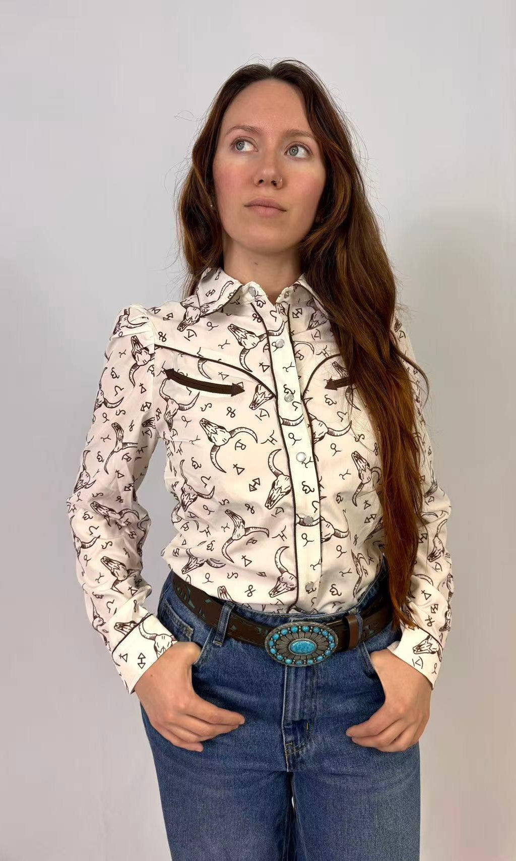 Woman wearing a black and white western print patterned blouse and blue jeans against a plain background
