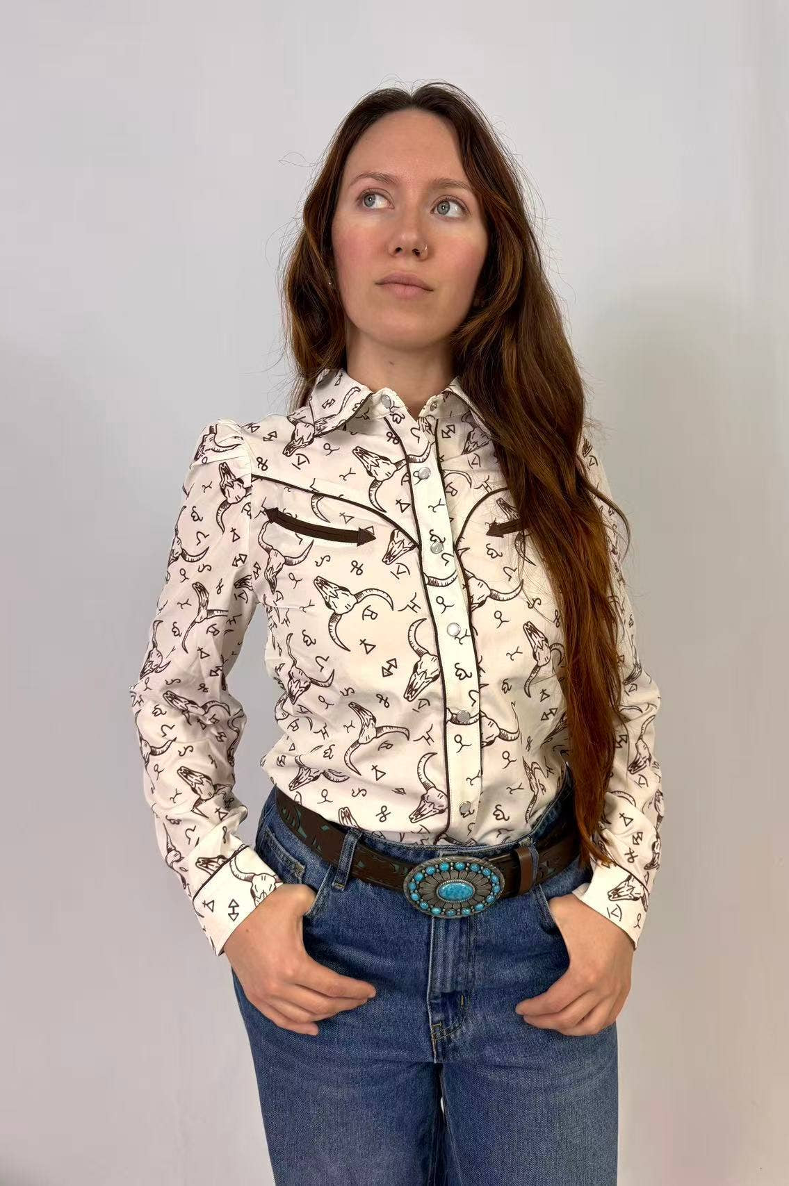 Woman wearing a black and white western print patterned blouse and blue jeans against a plain background
