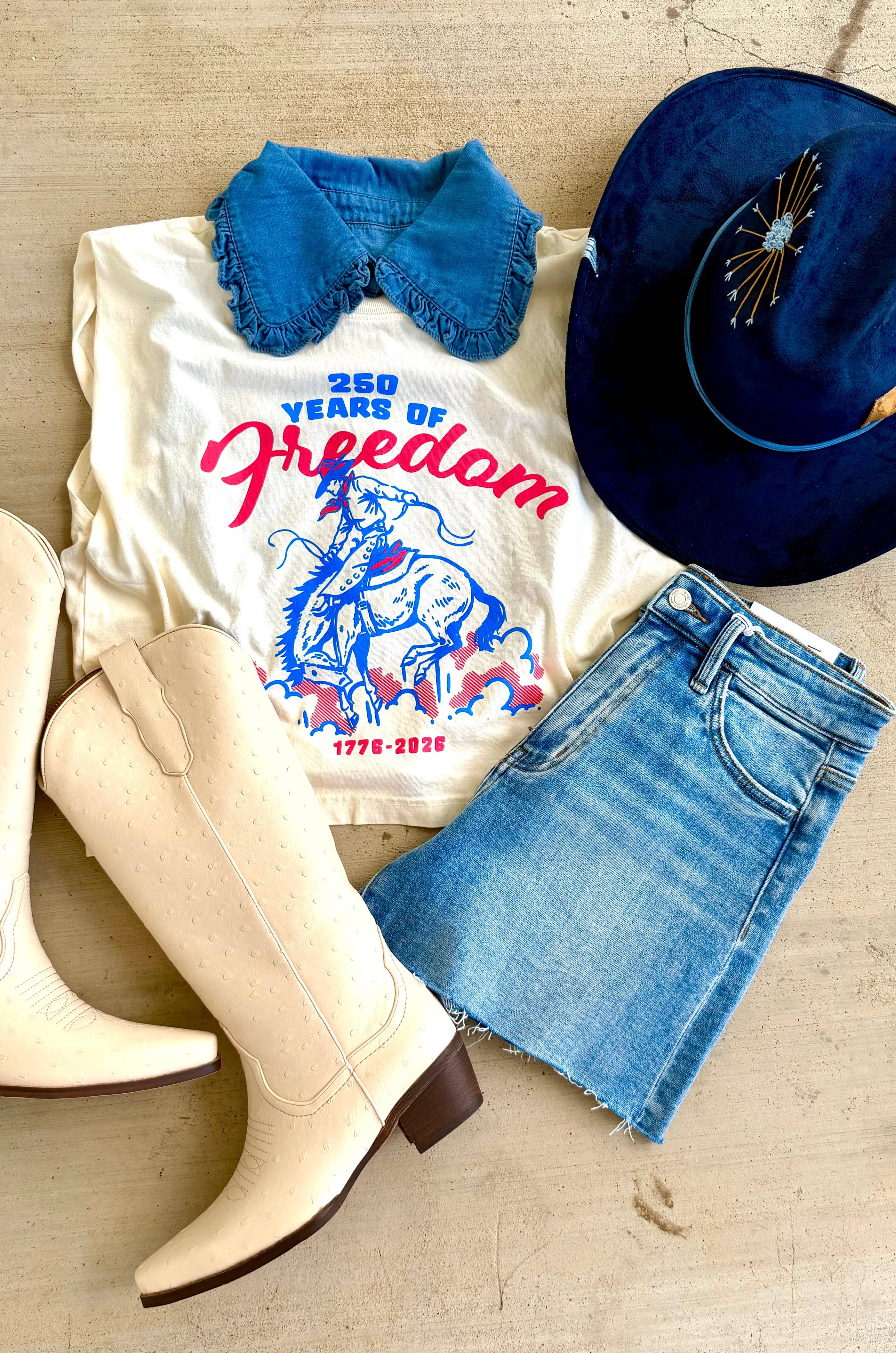 White boots, white t-shirt with graphic design, blue denim shorts, blue hat on a wooden surface