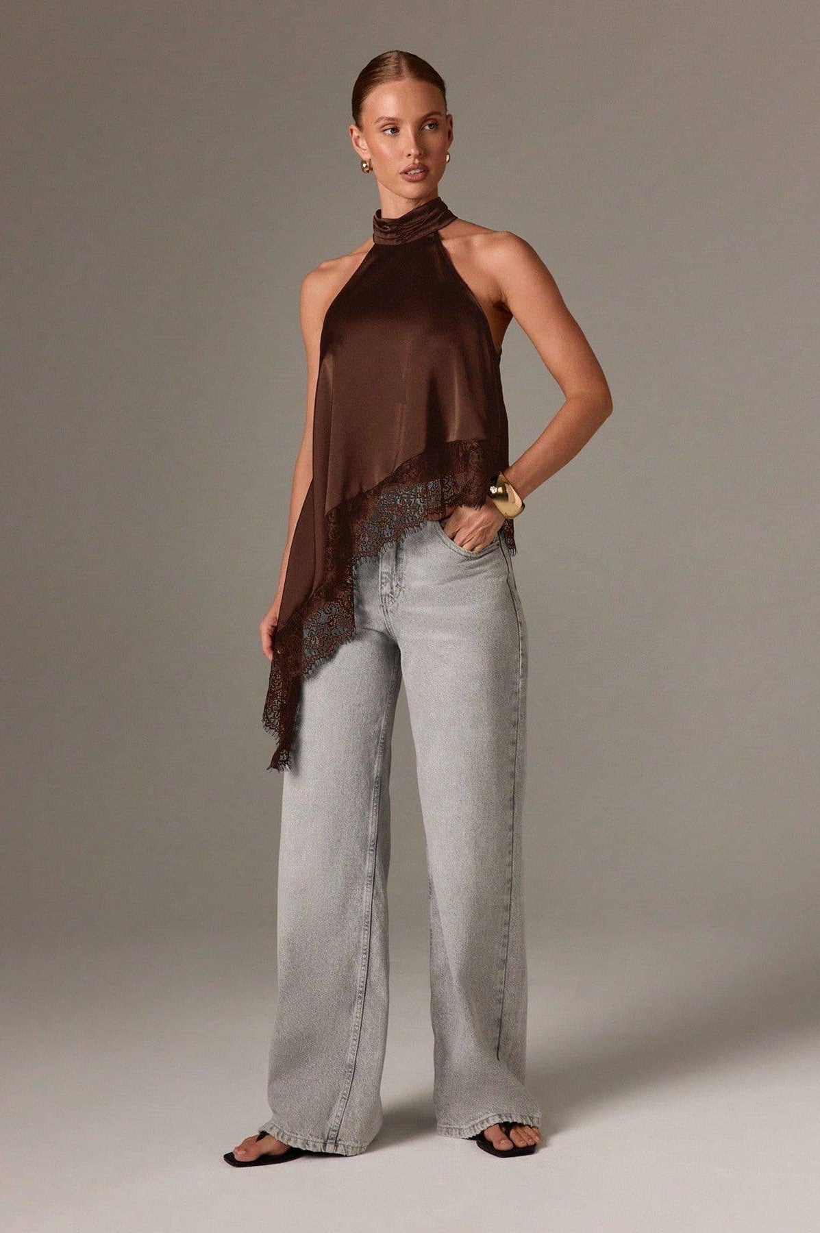 Woman wearing a brown halter top and light gray pants against a neutral background