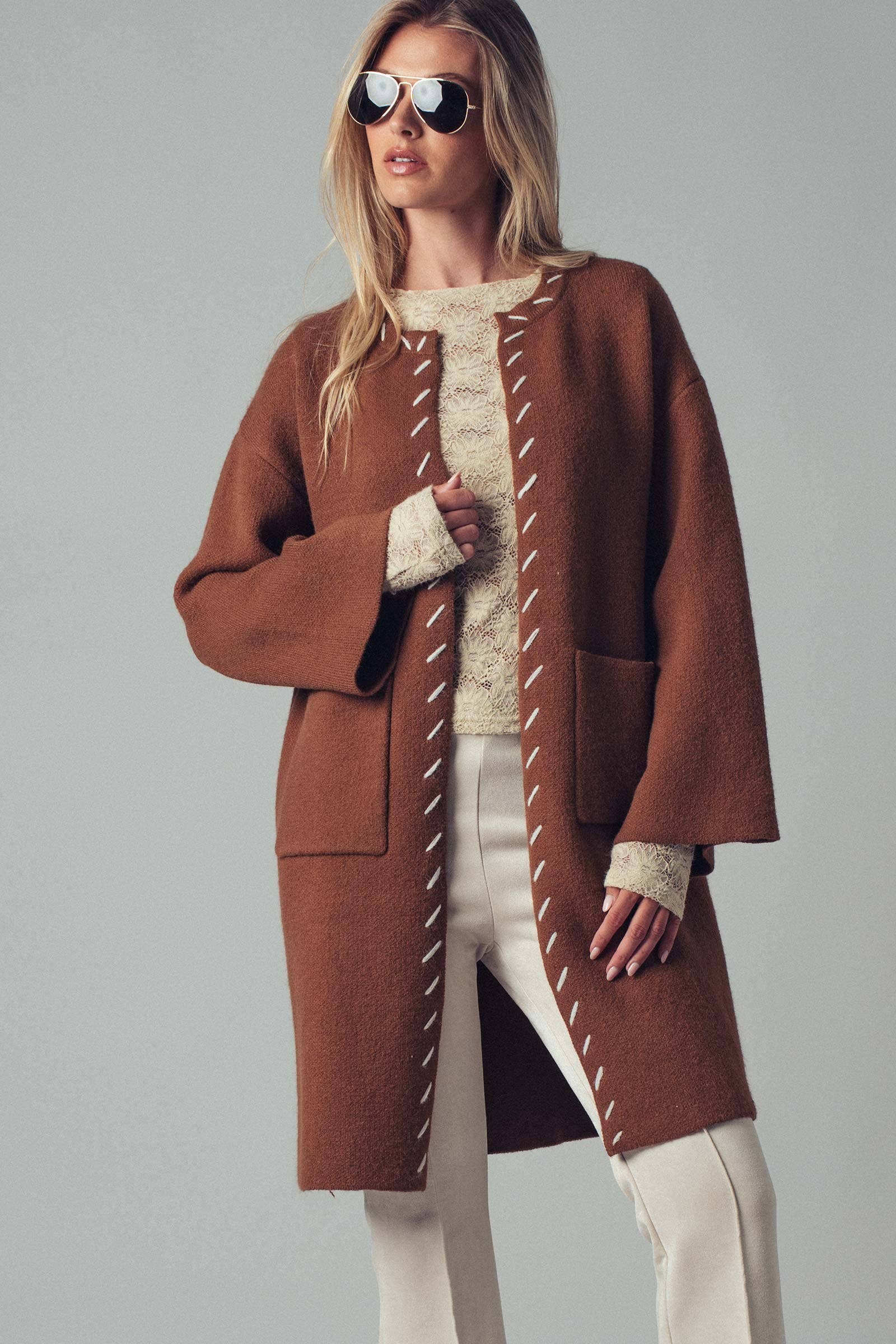 Woman wearing a brown open coat with white bold stitching trim