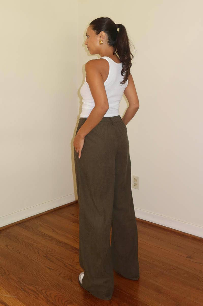 Person wearing a white top and brown high-waisted pants in a room with wooden flooring.
