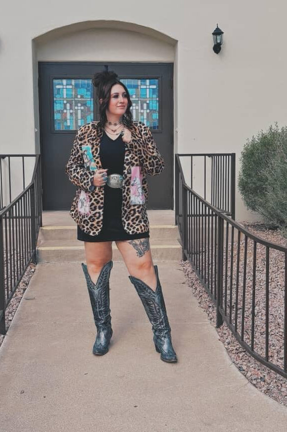 Person wearing a leopard print jacket and black boots standing in front of a building entrance.