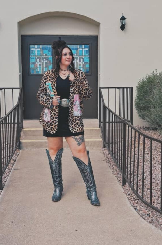 Person wearing a leopard print jacket and black boots standing in front of a building entrance.