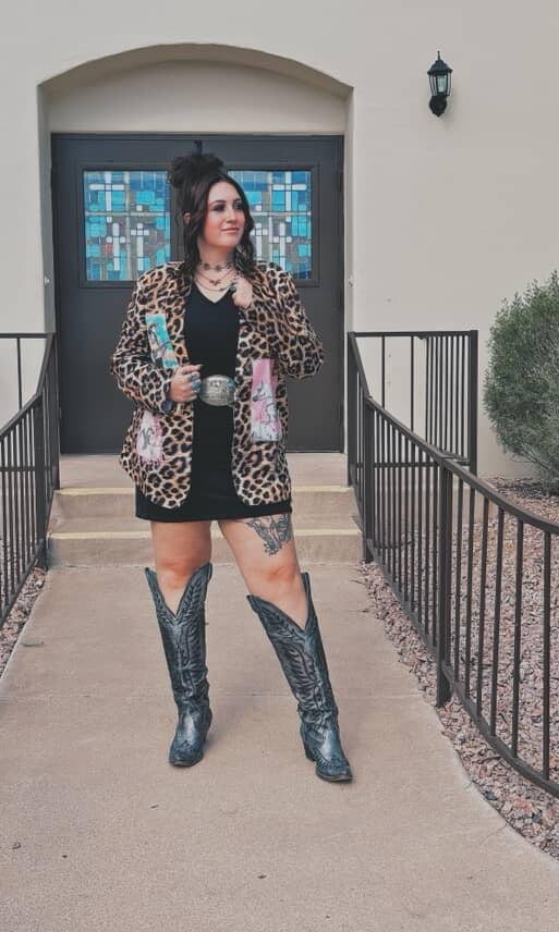Person wearing a leopard print jacket and black boots standing in front of a building entrance.