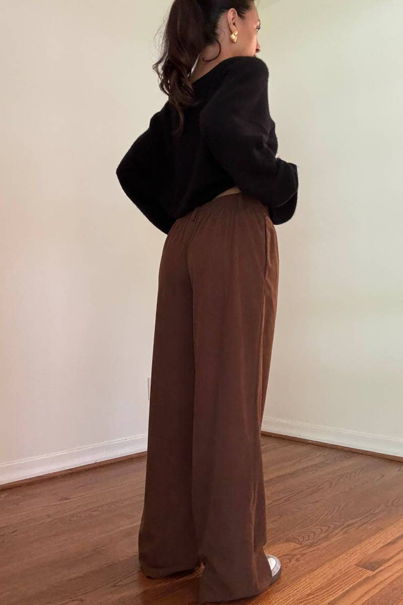 Person wearing a black top and brown corduroy wide leg pants standing indoors.