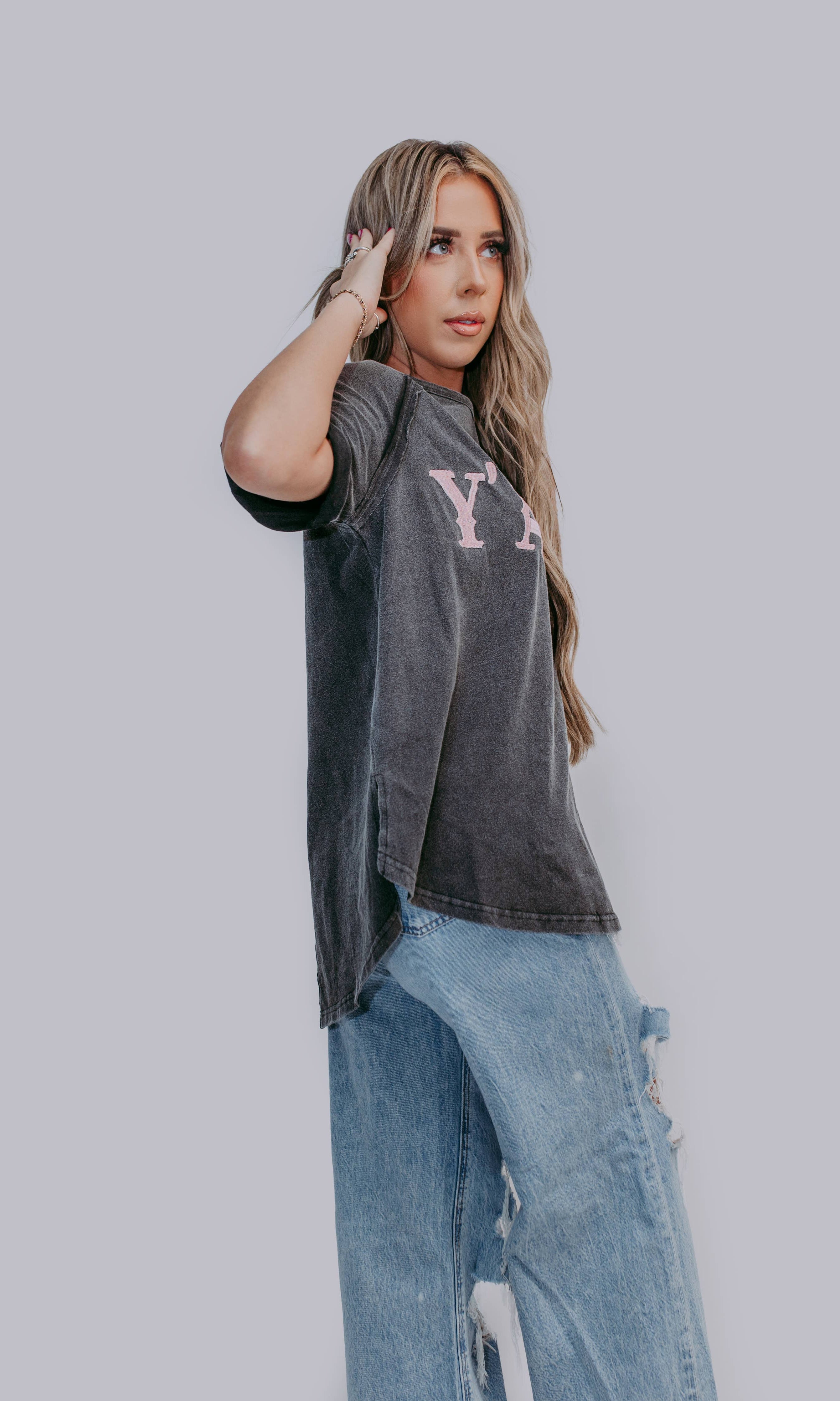 Woman wearing a dark gray t-shirt with logo and light blue jeans against a plain background