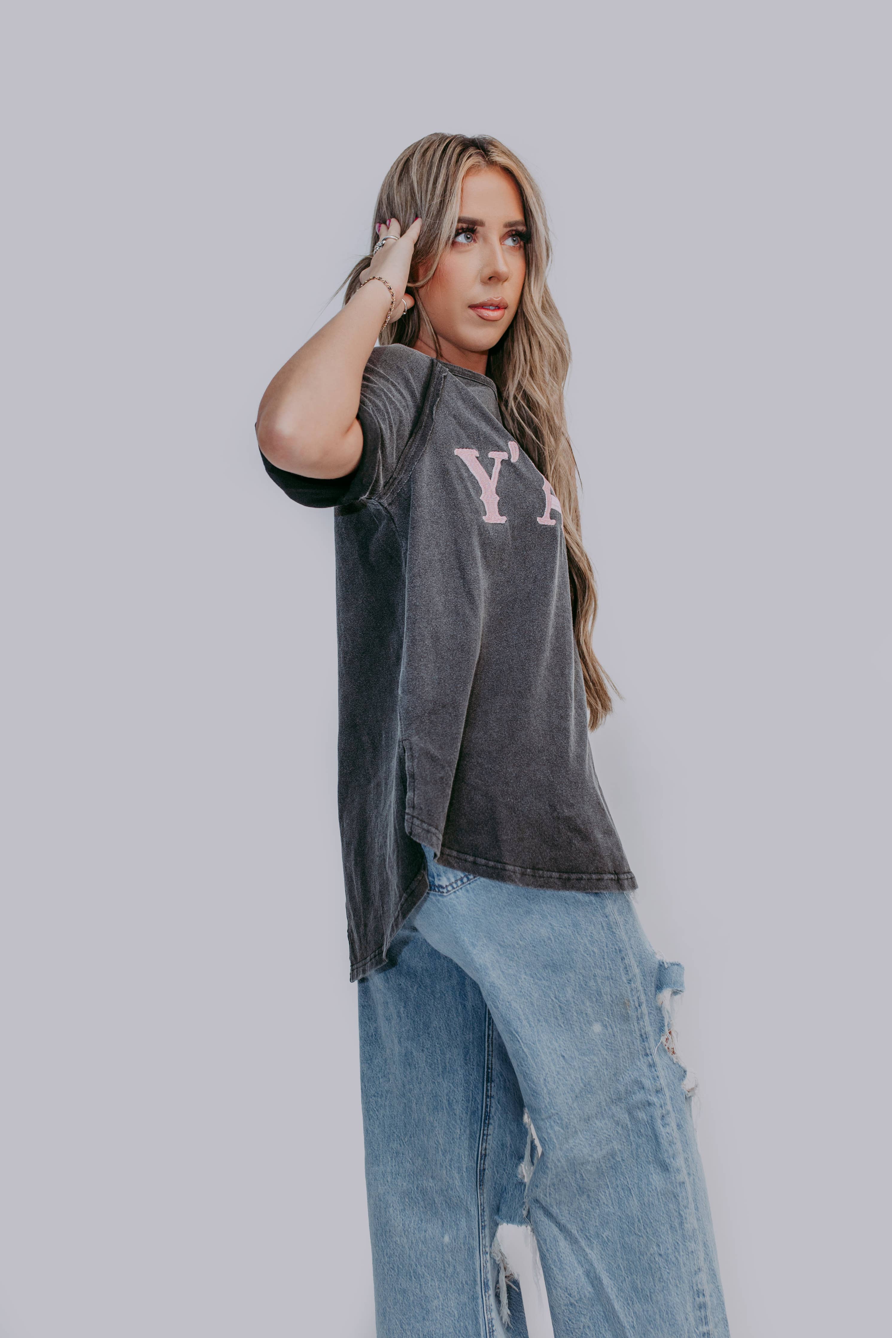 Woman wearing a dark gray t-shirt with logo and light blue jeans against a plain background