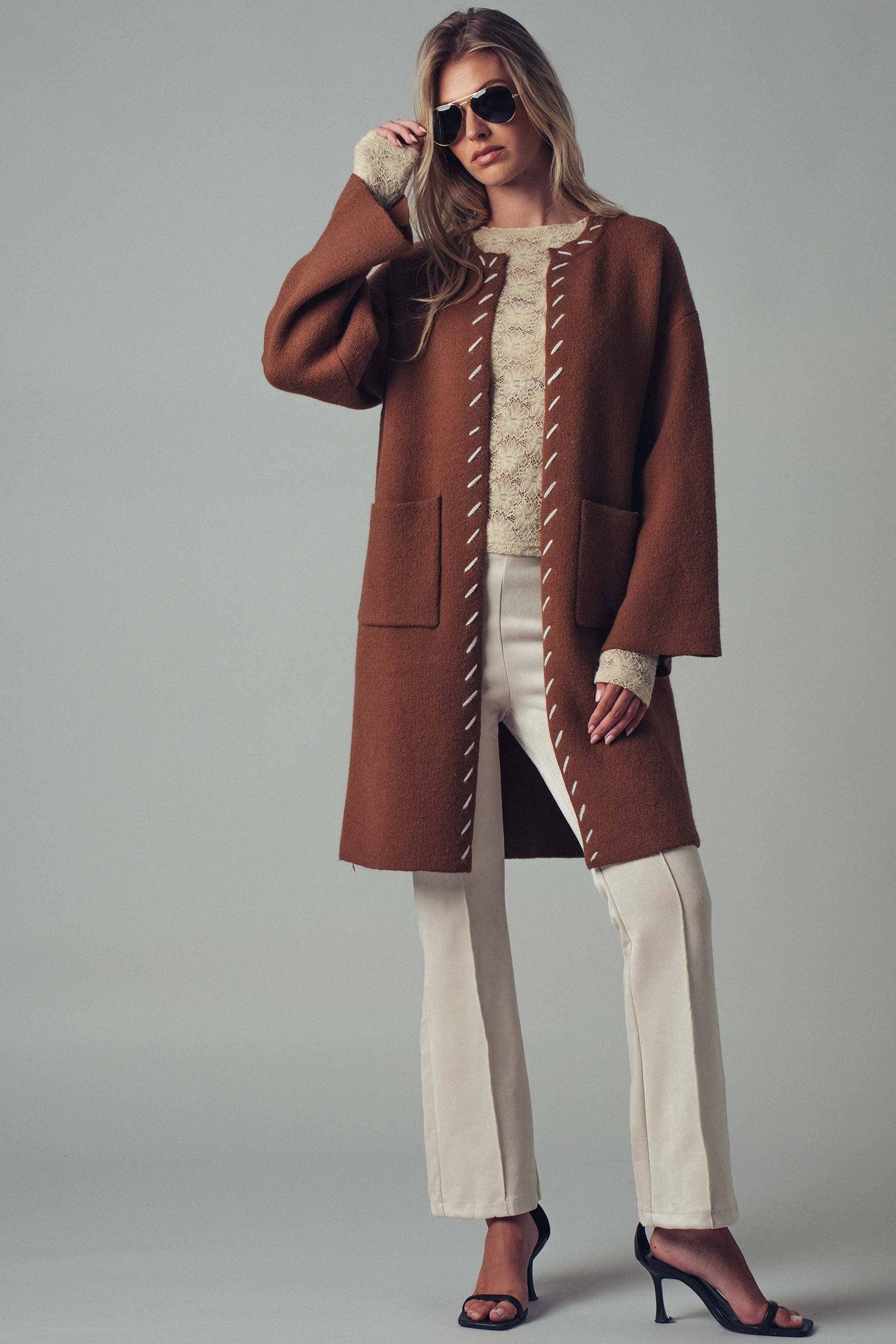 Woman wearing a brown open coat with white bold stitching trim