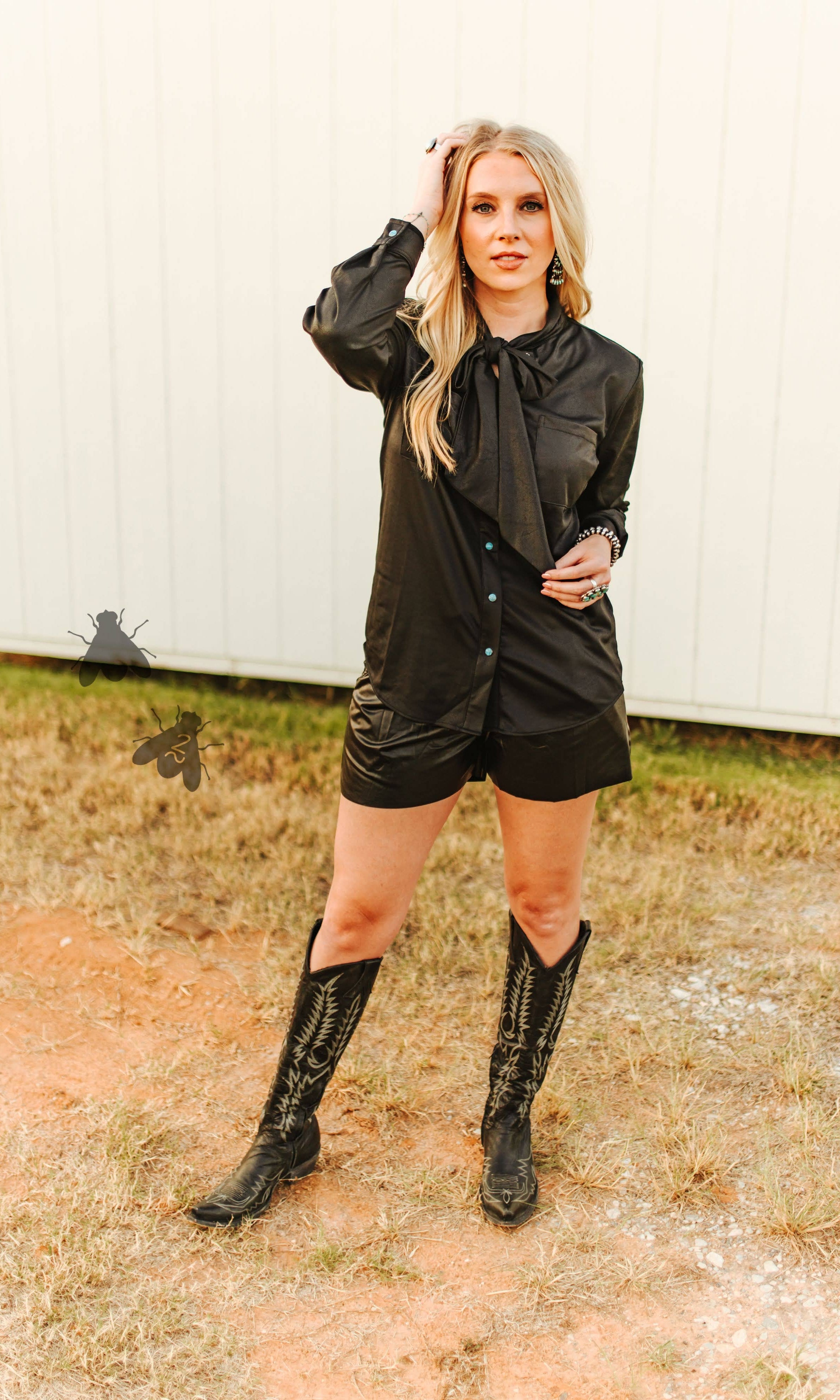 Woman in a black outfit with knee-high boots standing outdoors.
