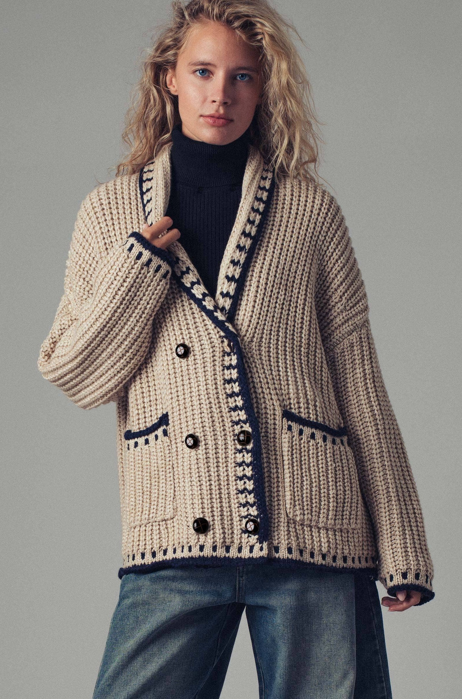 Woman wearing a beige knitted cardigan with black buttons on a gray background