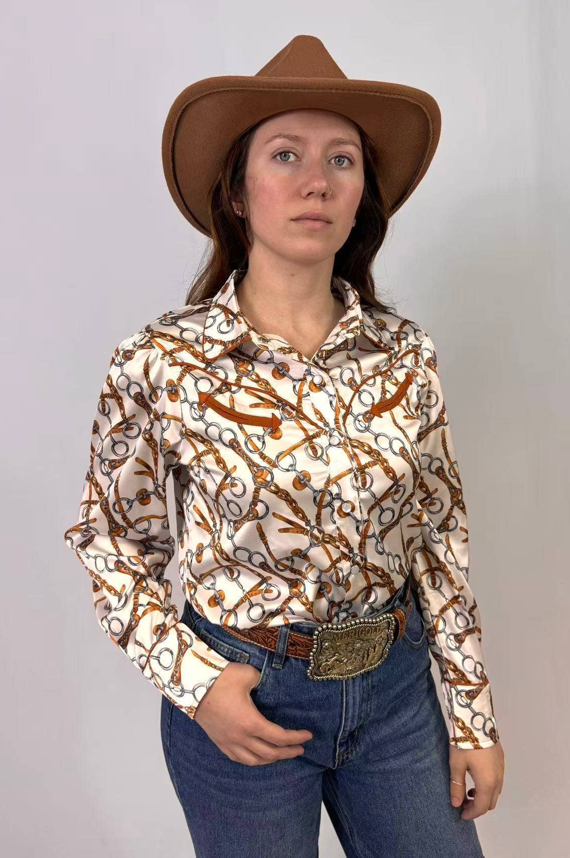 Person wearing a patterned shirt, jeans, and a cowboy hat against a plain background