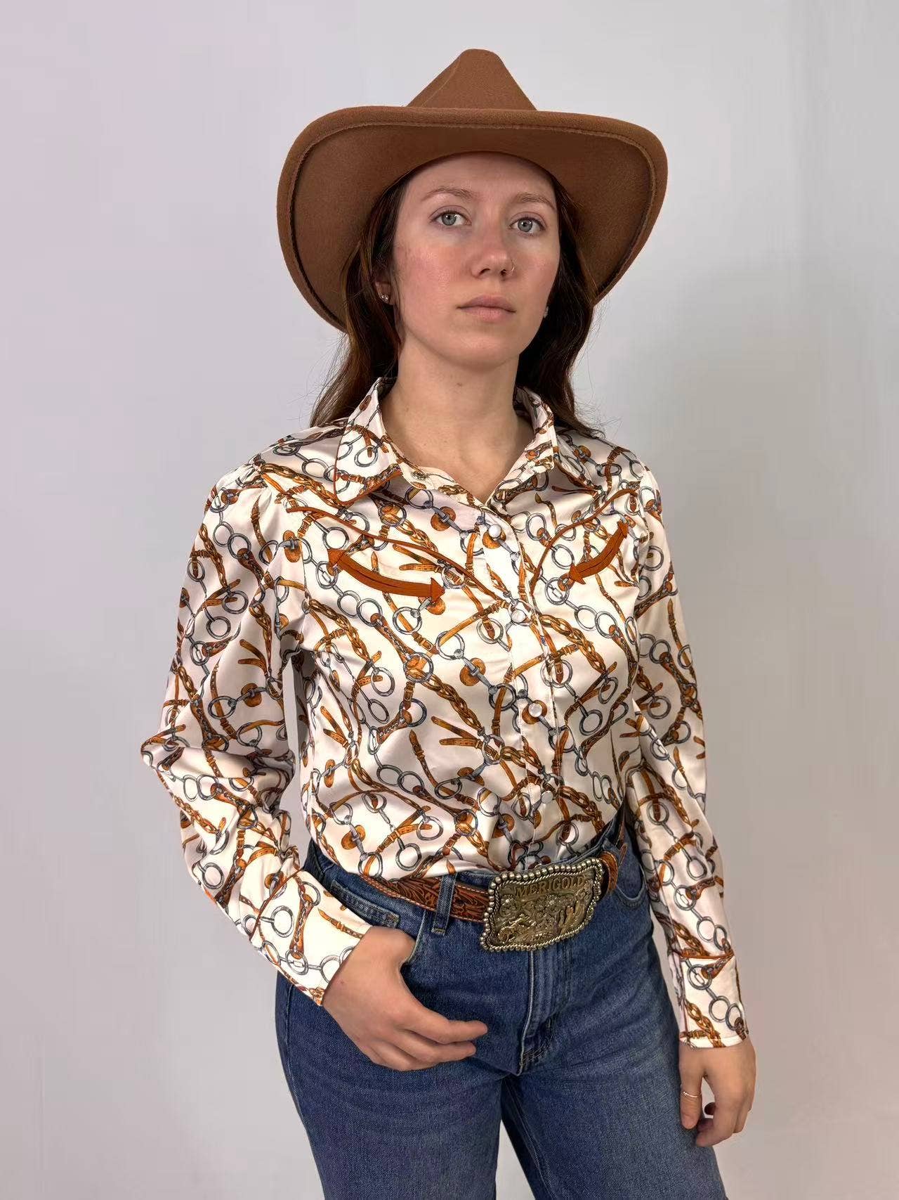 Person wearing a patterned shirt, jeans, and a cowboy hat against a plain background
