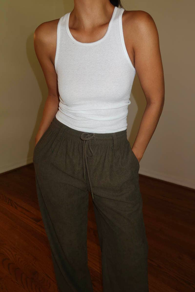 Person wearing a white tank top and brown corduroy drawstring pants indoors.