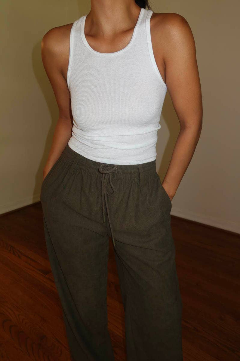 Person wearing a white tank top and brown corduroy drawstring pants indoors.