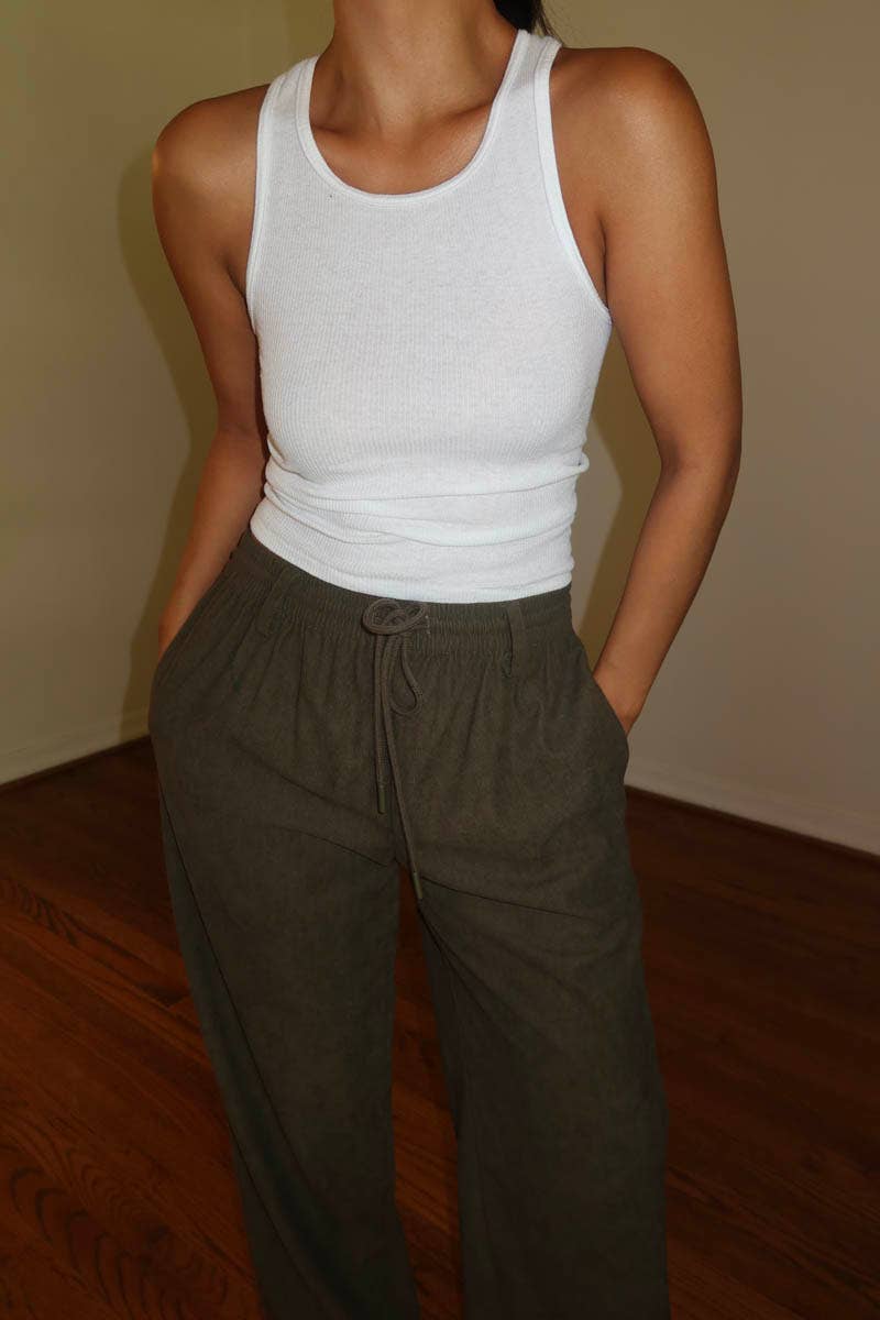 Person wearing a white tank top and brown corduroy drawstring pants indoors.
