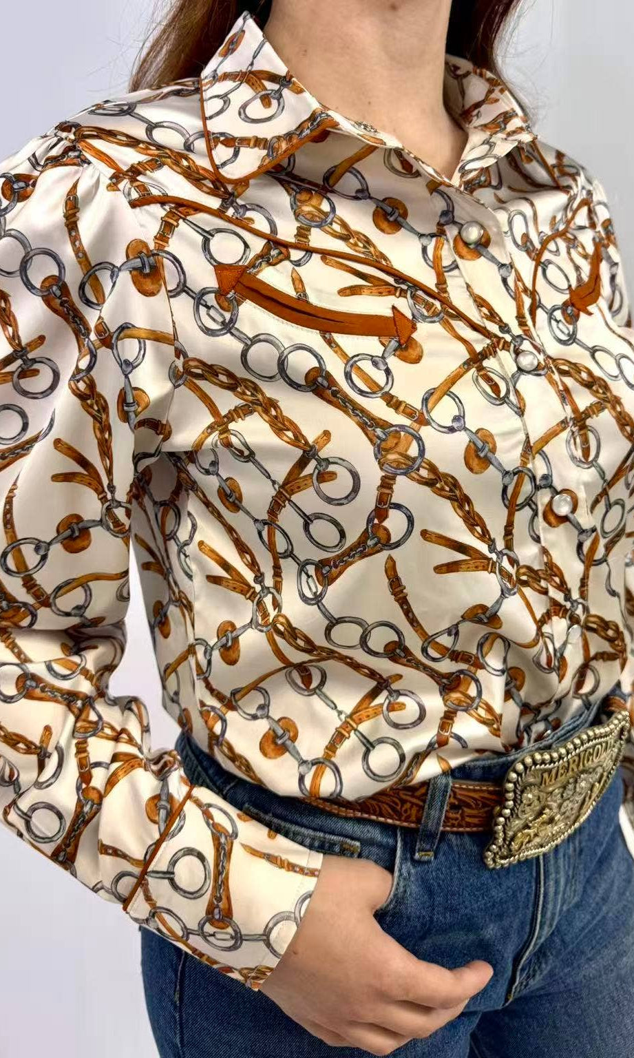 Person wearing a patterned shirt with long sleeves and jeans on a plain background