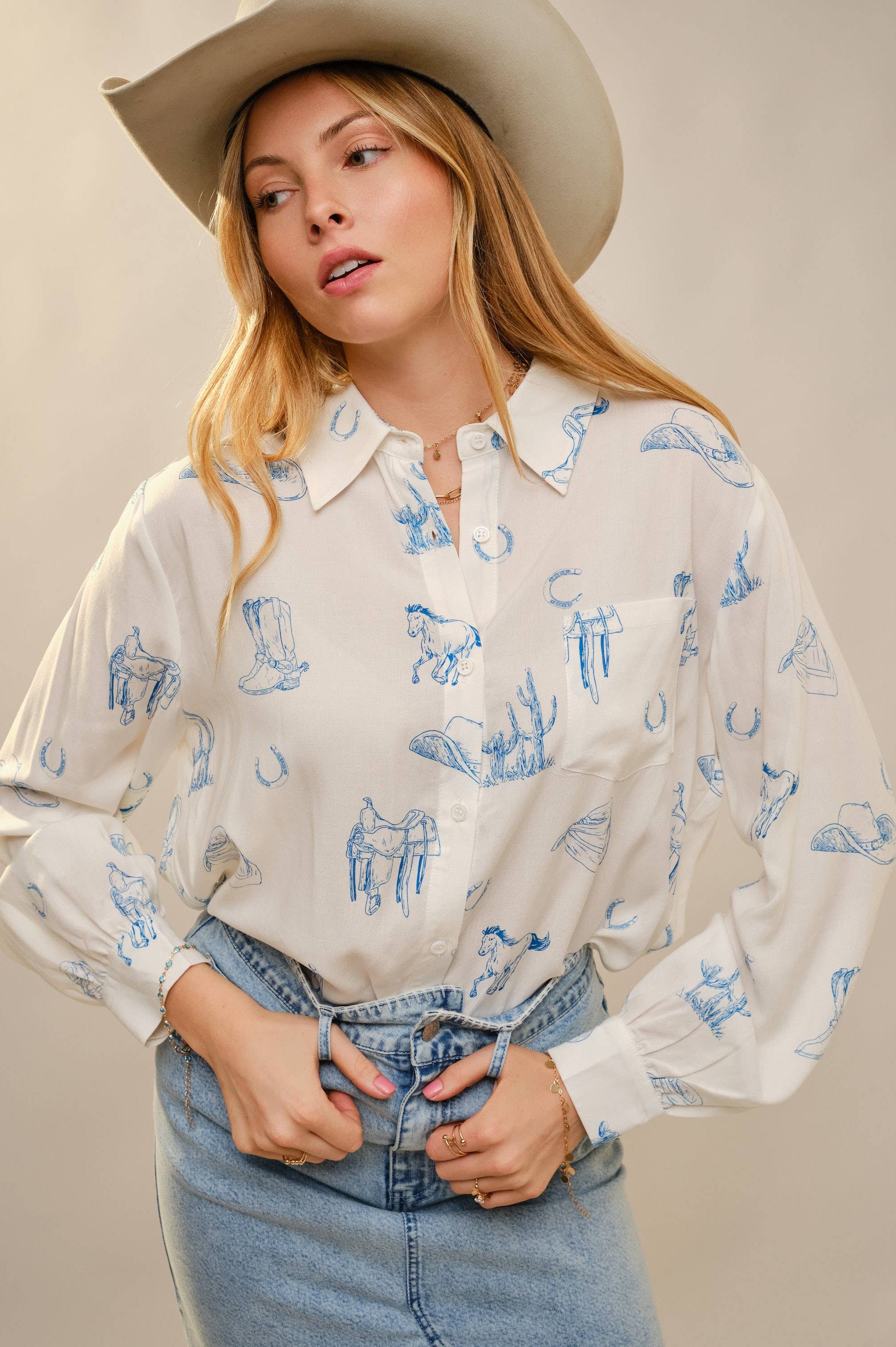Woman wearing a white blouse with blue patterns and a cowboy hat against a plain background