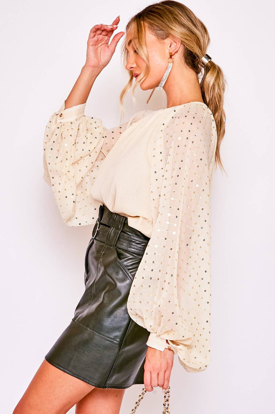 Woman wearing a beige blouse with long sleeves and a black leather skirt against a white background
