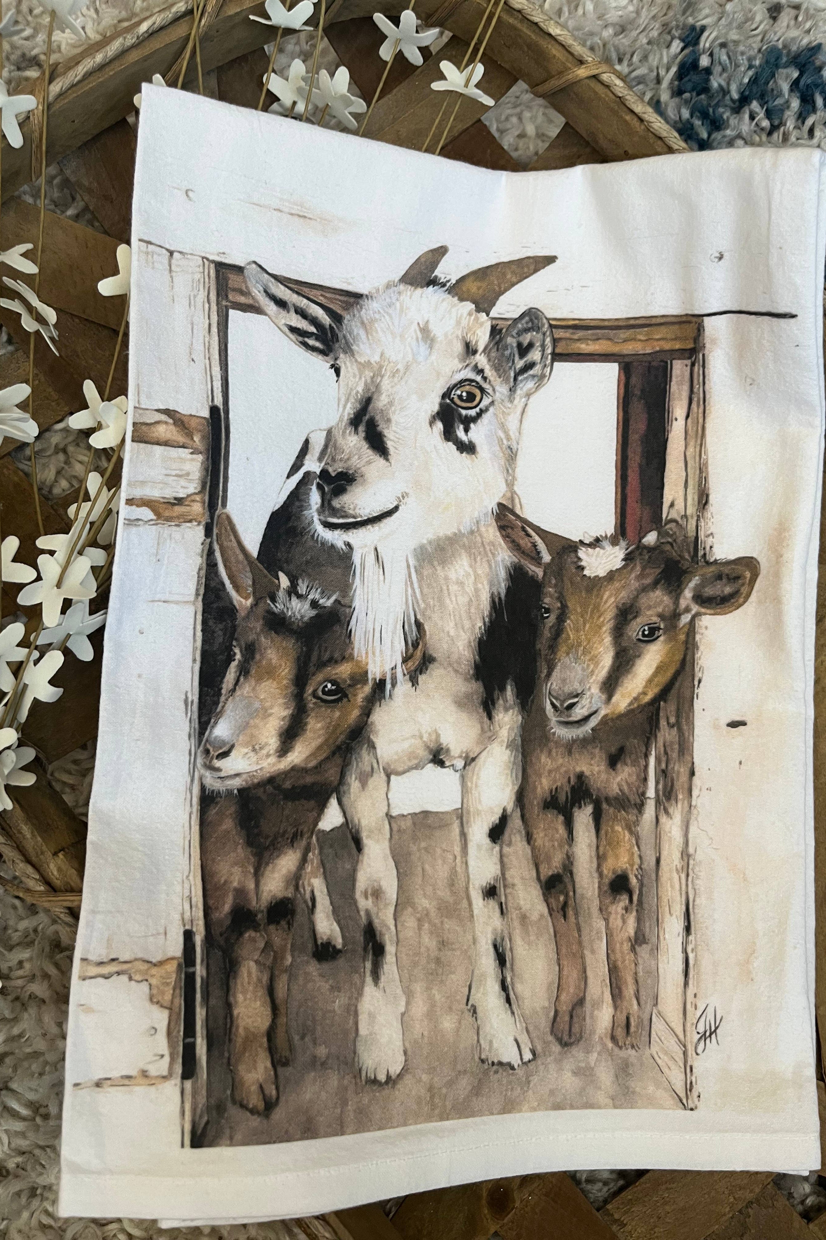 Kitchen towel with Illustration of three goats peeking out from a wooden frame on a textured surface.