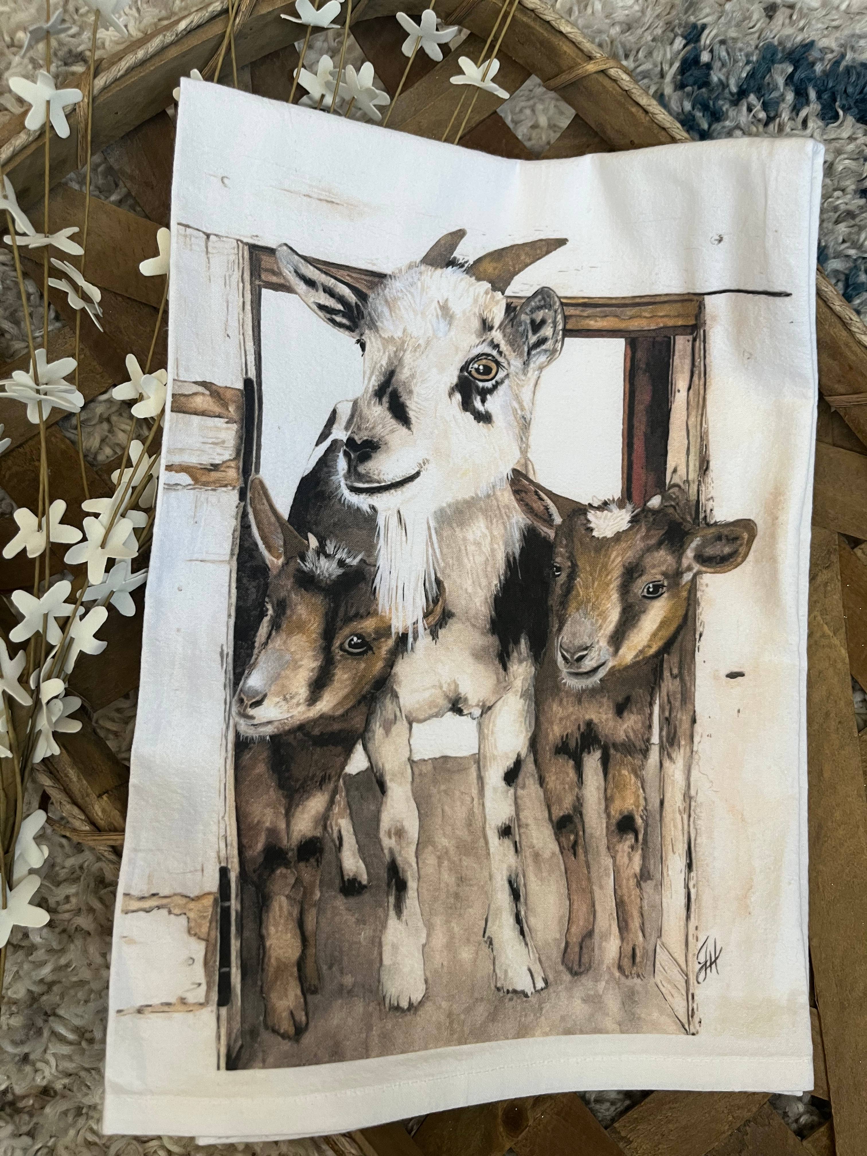 Kitchen towel with Illustration of three goats peeking out from a wooden frame on a textured surface.
