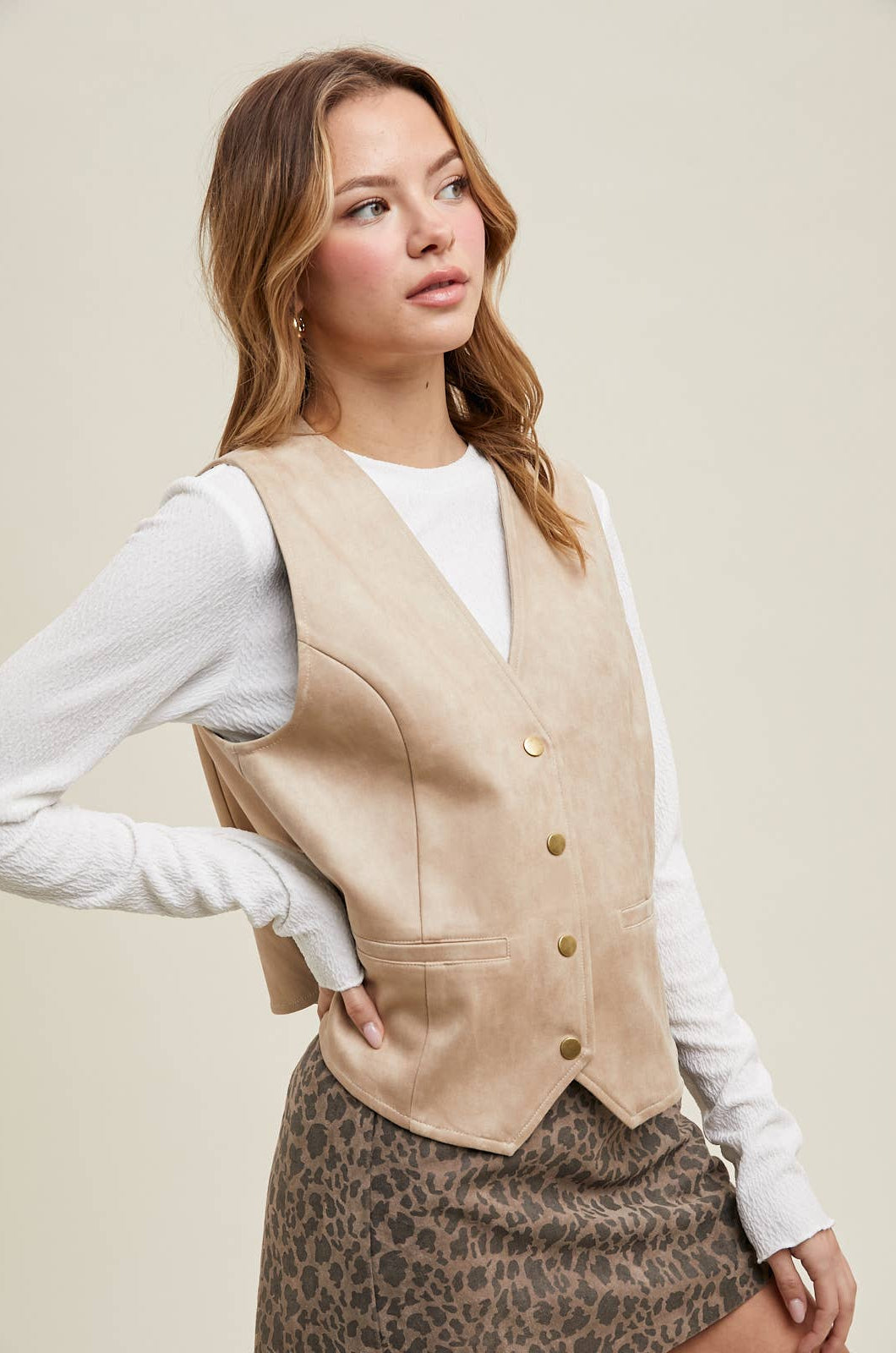 A woman wearing a stone suede snap-up vest over a white shirt, paired with a leopard print mini skirt.