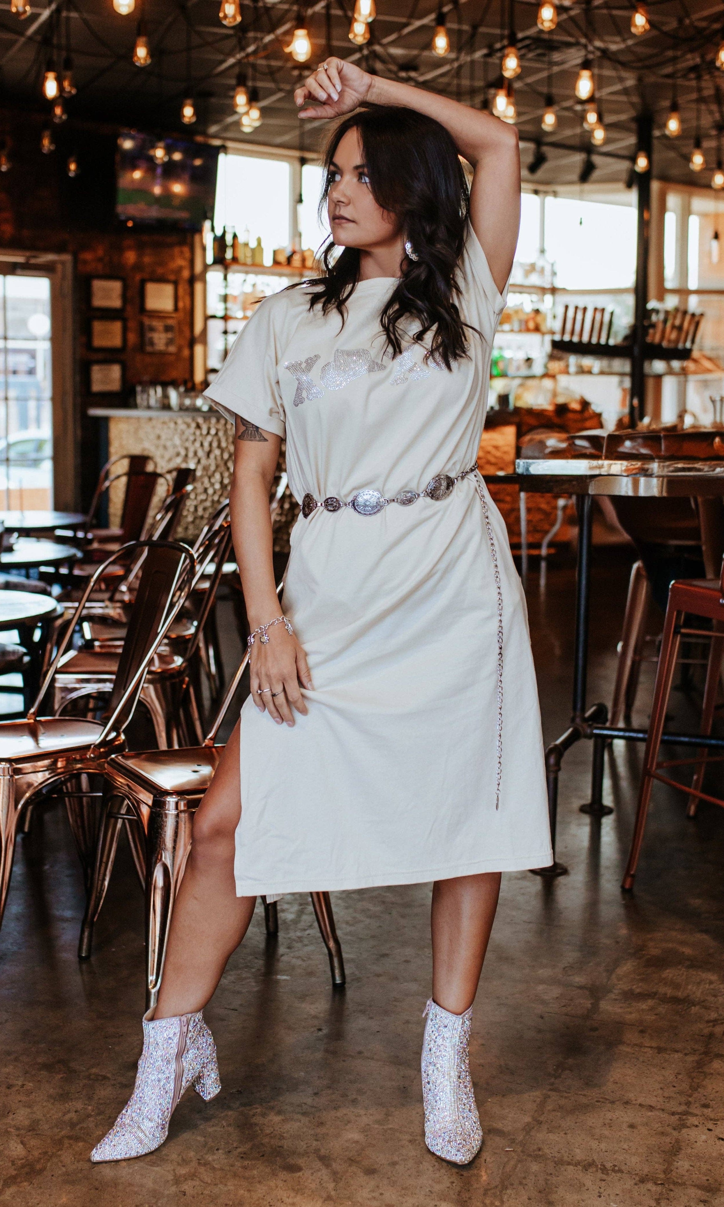 Woman in a white dress posing in a restaurant with wooden floors and tables.