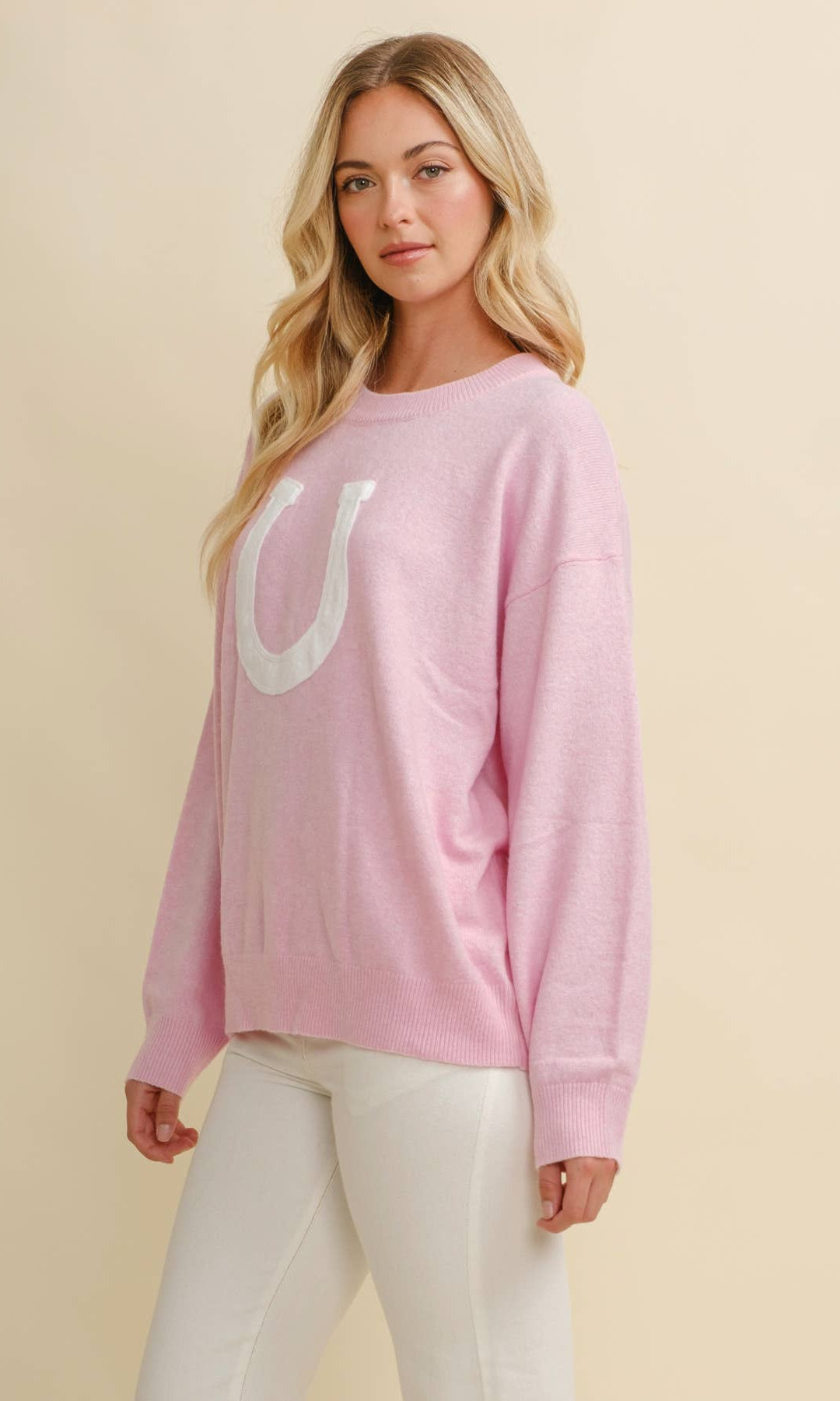 Woman wearing a pink sweater with a large white horse shoe on a beige background