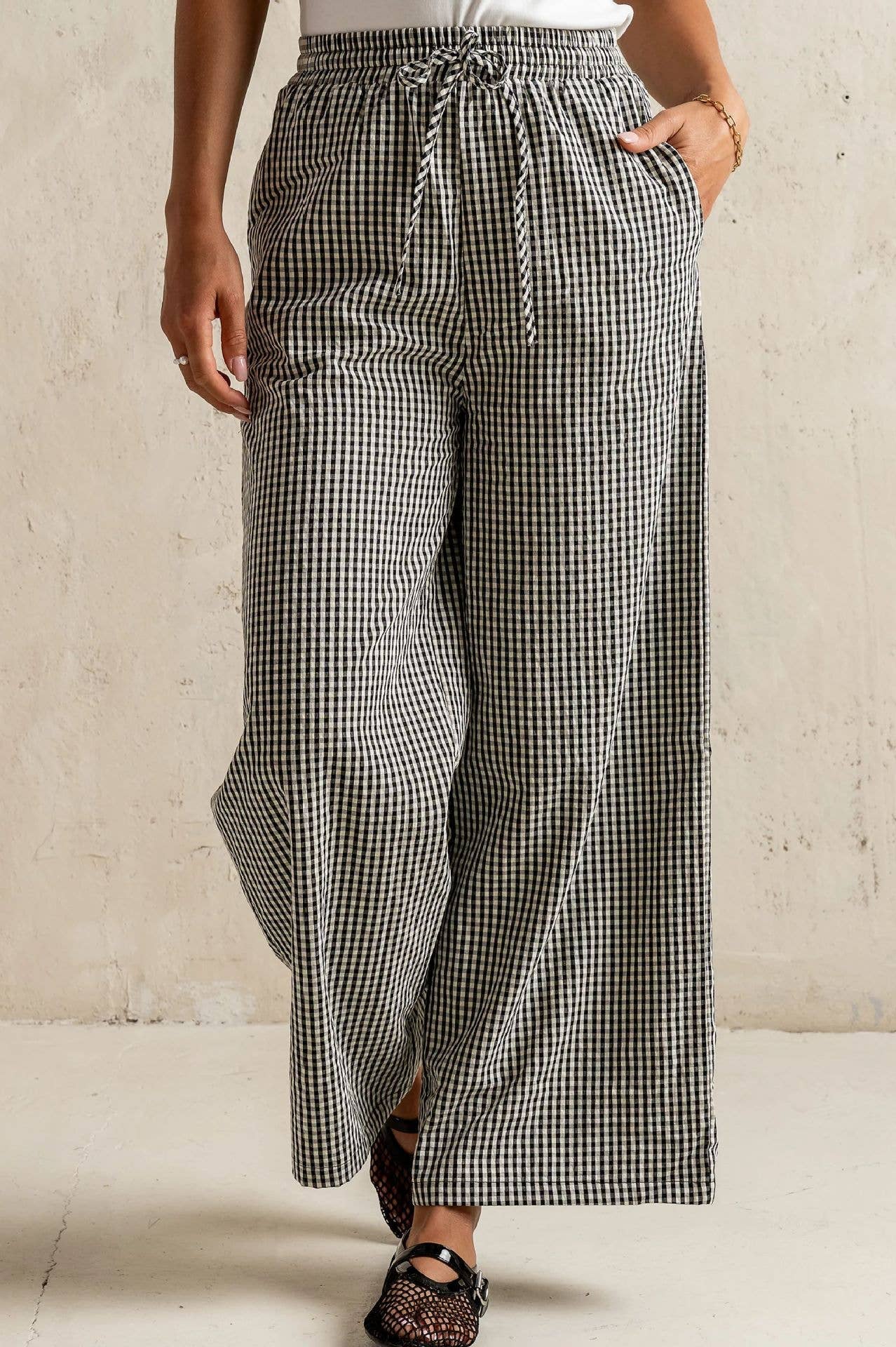 Person wearing black and white checkered pants against a beige wall.