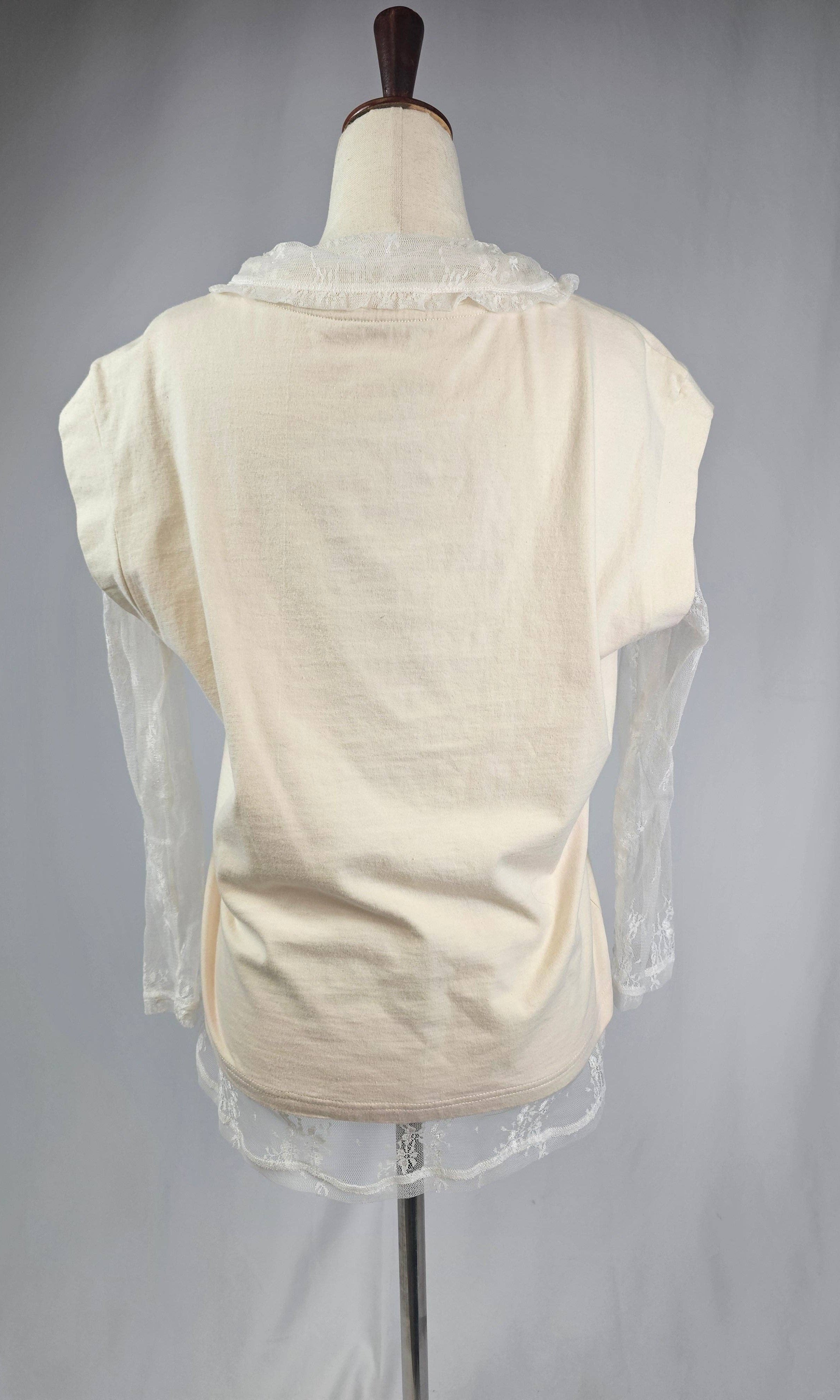 Mannequin wearing a cream-colored garment with sheer sleeves against a plain background