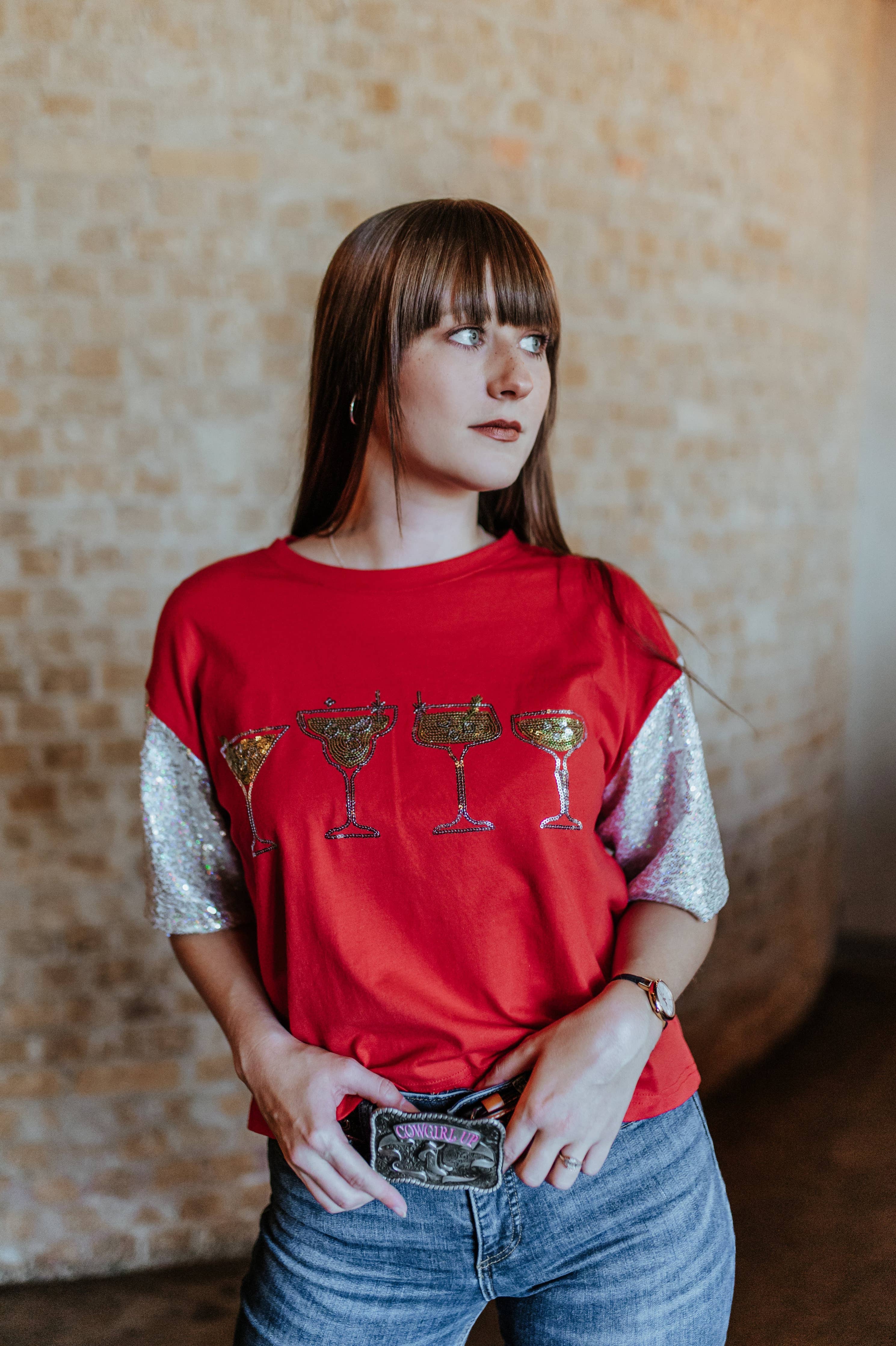 Woman wearing a red shirt with graphic design, standing against a textured wall.