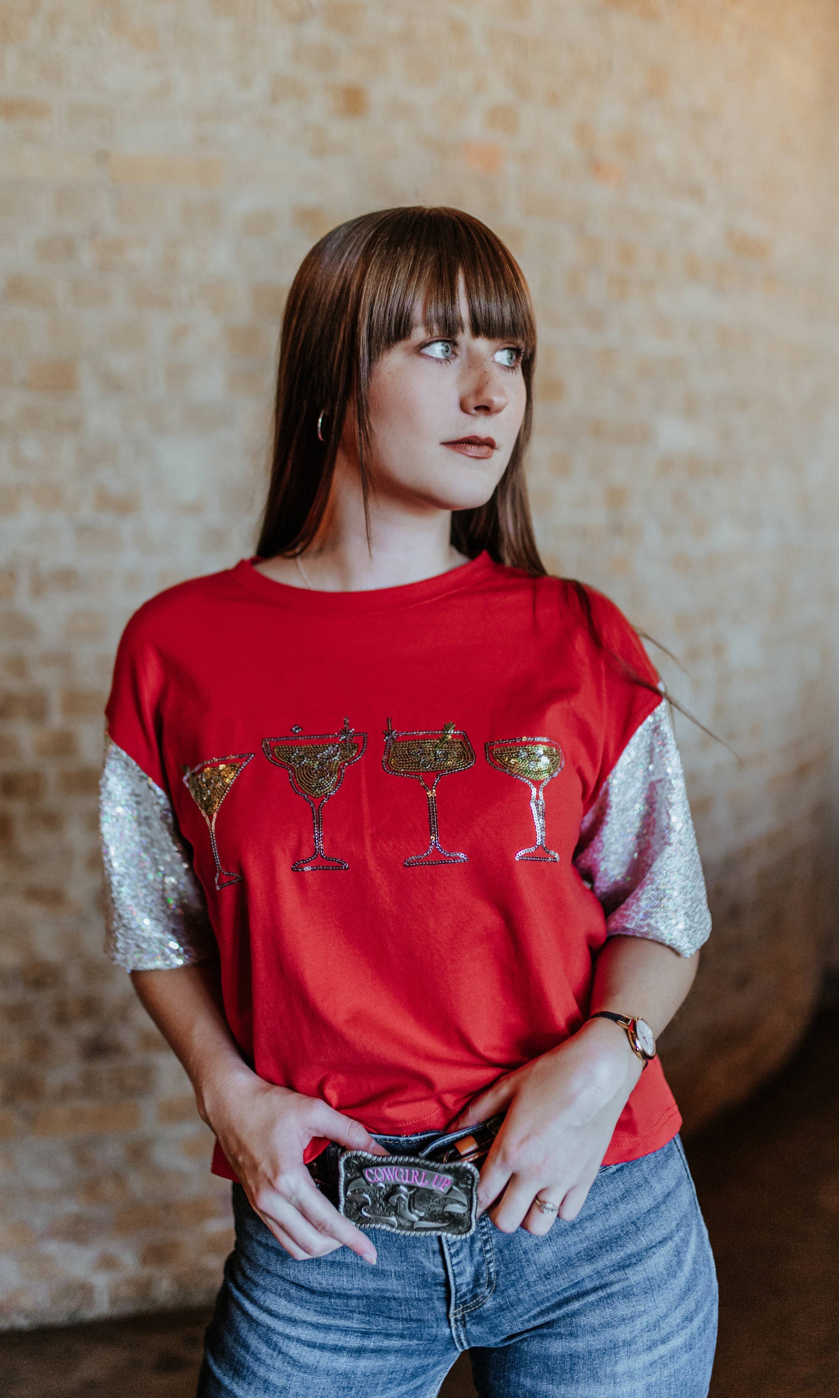 Woman wearing a red shirt with graphic design, standing against a textured wall.