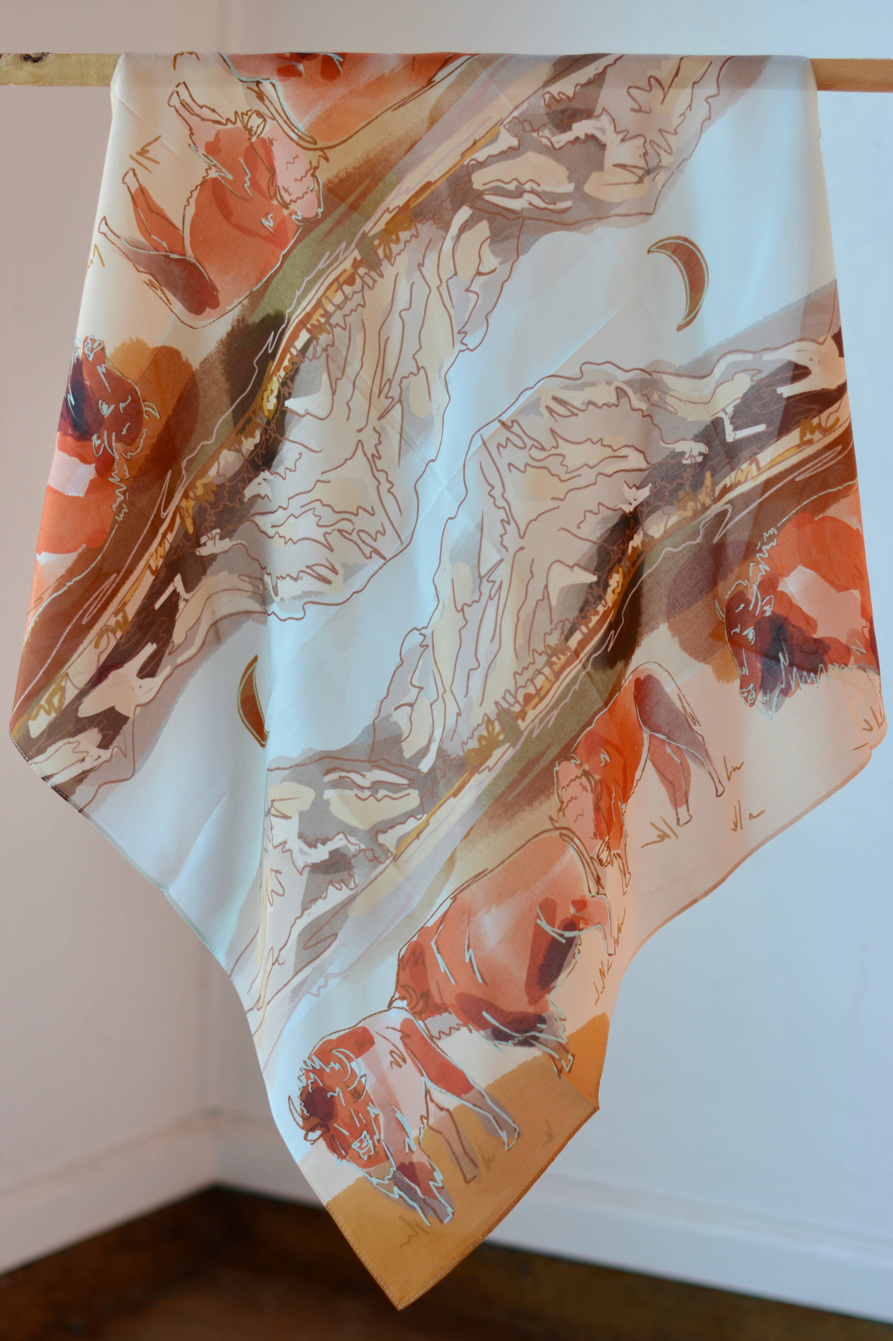 Silk scarf with abstract animal design on a wooden hanger against a white wall.