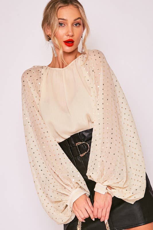 Woman wearing a beige blouse with gold sequins and black skirt on a white background