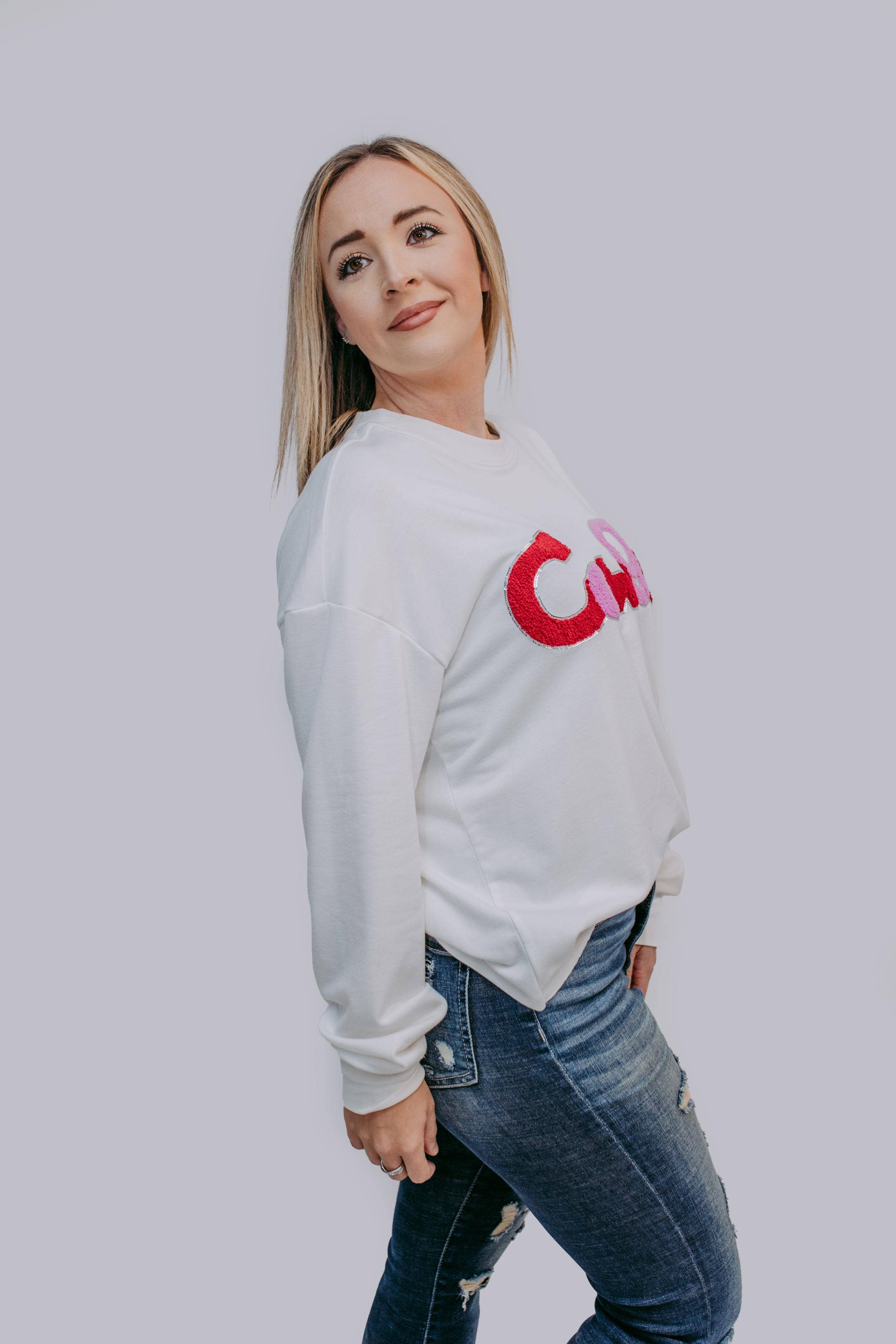 Woman wearing a white sweatshirt with a red logo on a plain background