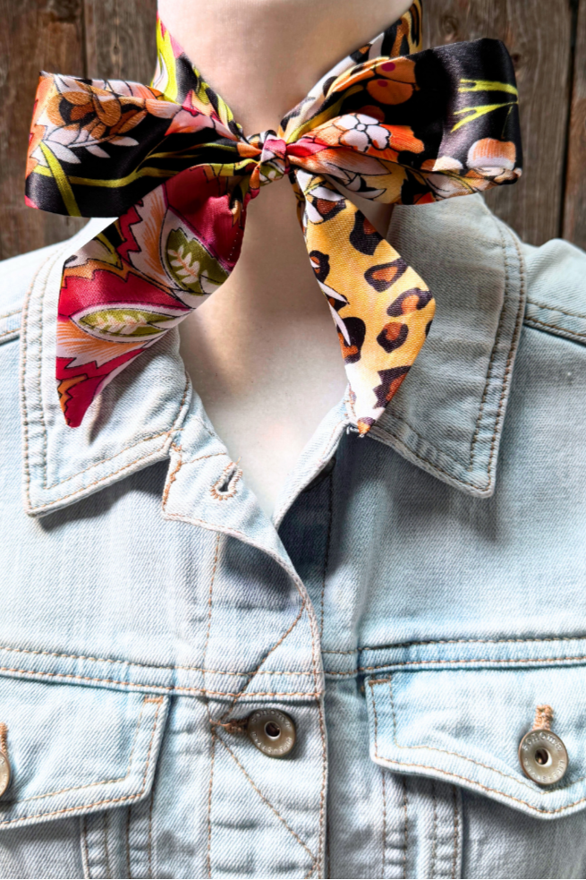 Mannequin wearing a denim jacket with a colorful scarf tied around the neck against a wooden background