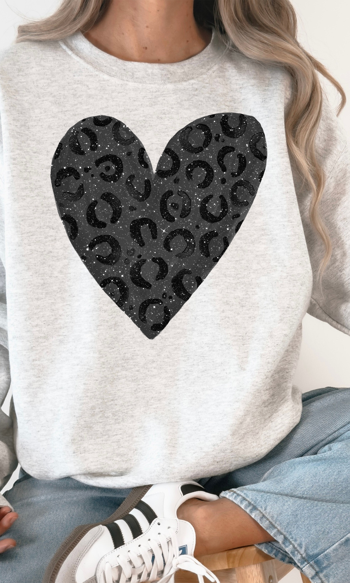 Gray sweatshirt with a black leopard heart-shaped pattern worn by a person sitting on a white surface.