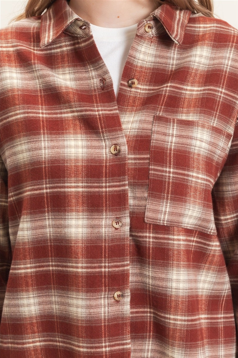 A close-up of a person wearing a rust red and cream plaid button-up shirt over a white undershirt.