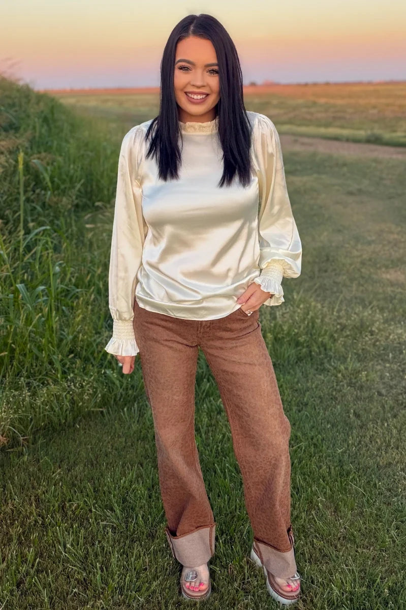 Woman wearing Sand Cat Cuffed Jeans featuring a subtle leopard print, high-rise wide-leg fit, and statement contrast cuff styled with a cream satin blouse.