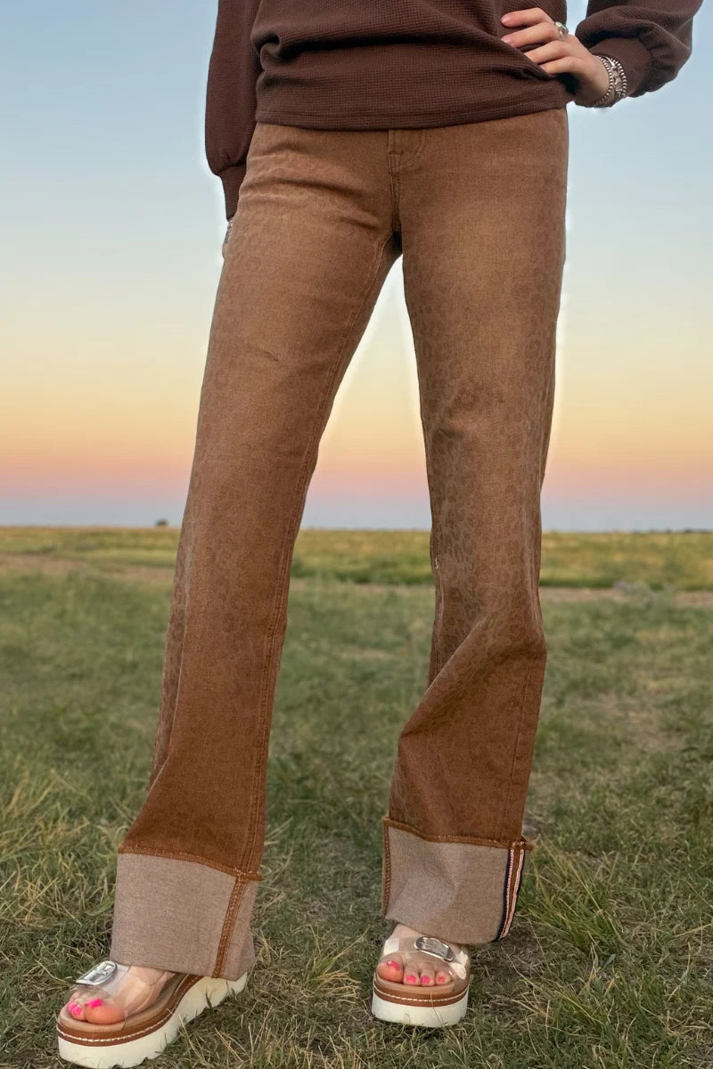 Close-up of Sand Cat Cuffed Jeans showing the tonal leopard print, high-rise waistband, front pocket, button closure, and warm camel-brown wash.