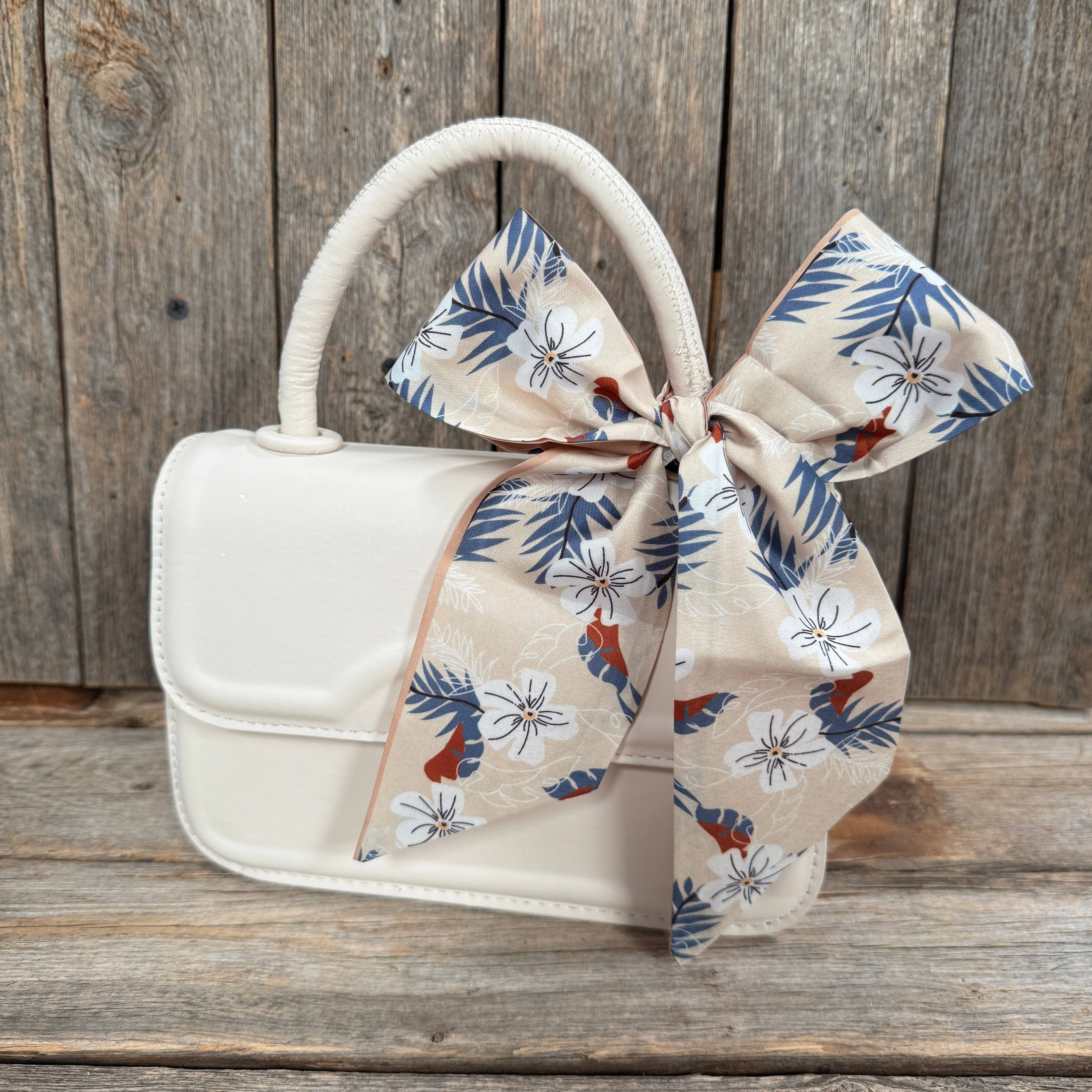 White handbag with a floral scarf ribbon on a wooden surface